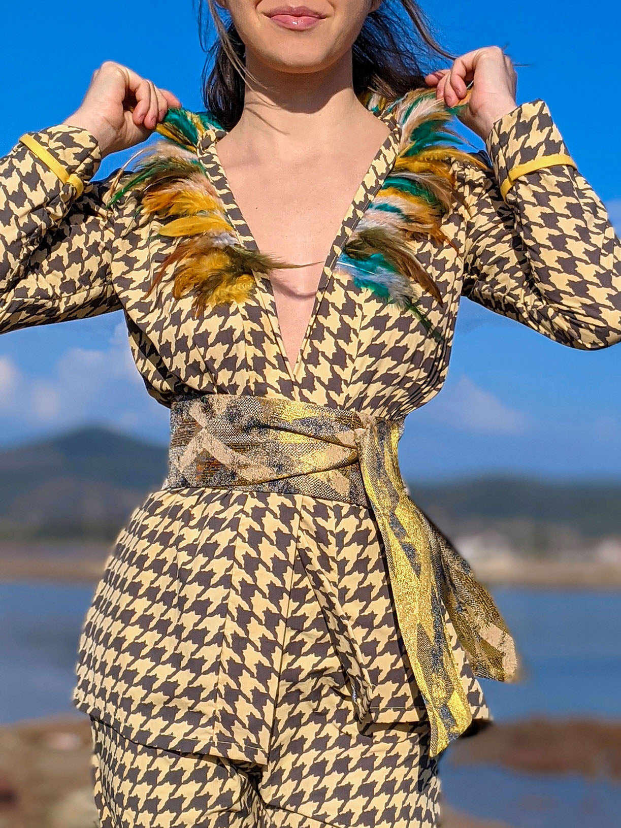 LAGINA jacket and pants suit featuring houndstooth pattern in yellow and tile brown, adorned with colorful feathers and shiny golden waistband.