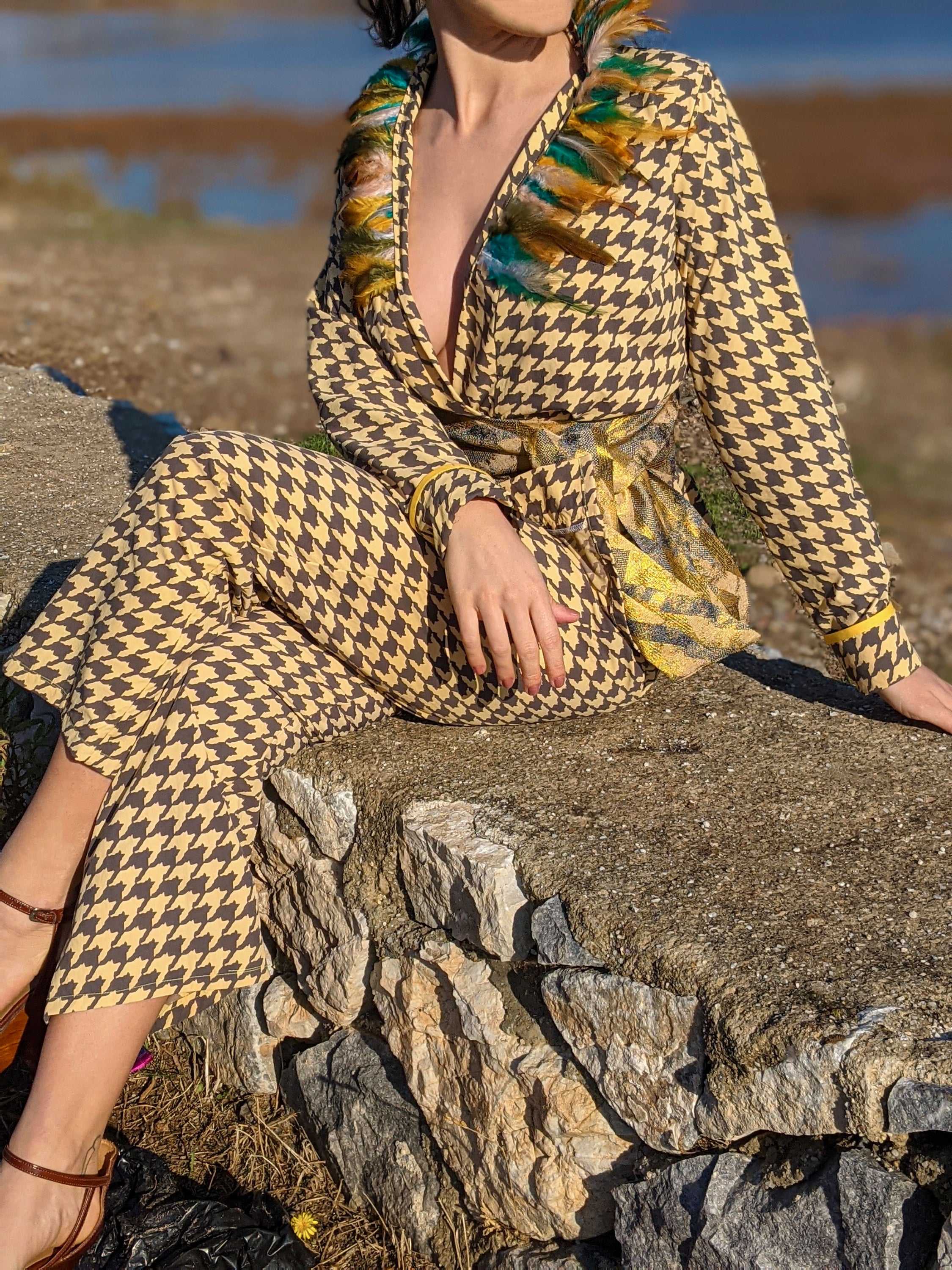 LAGINA jacket and pants suit featuring houndstooth pattern in yellow and tile brown, adorned with colorful feathers and shiny golden waistband.