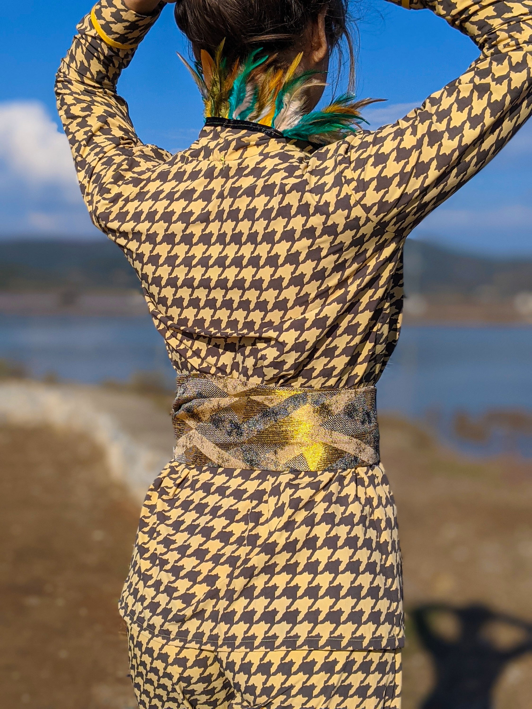 LAGINA jacket and pants suit featuring houndstooth pattern in yellow and tile brown, adorned with colorful feathers and shiny golden waistband.