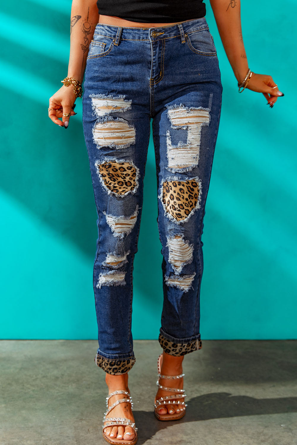 A pair of leopard patch distressed cuffed jeans displayed on a studio backdrop, showcasing their unique design and casual style.