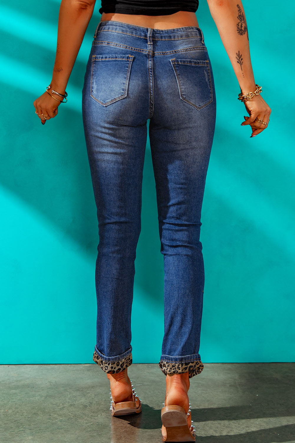 A pair of leopard patch distressed cuffed jeans displayed on a studio backdrop, showcasing their unique design and casual style.