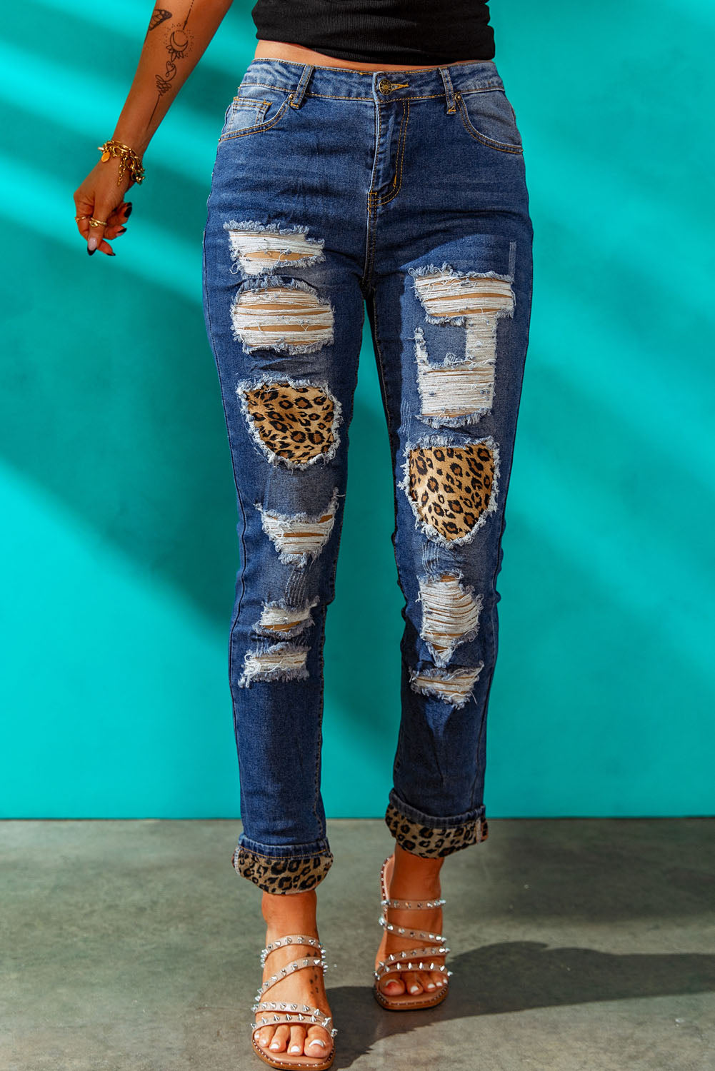 A pair of leopard patch distressed cuffed jeans displayed on a studio backdrop, showcasing their unique design and casual style.