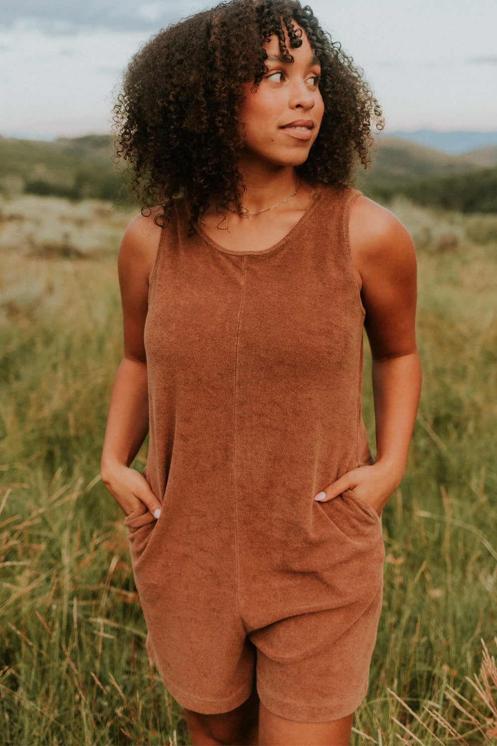 A stylish Let Go Romper made from 100% organic cotton, featuring a unique front seam and button clasp at the back, available in Brown, Olive, and Orange.