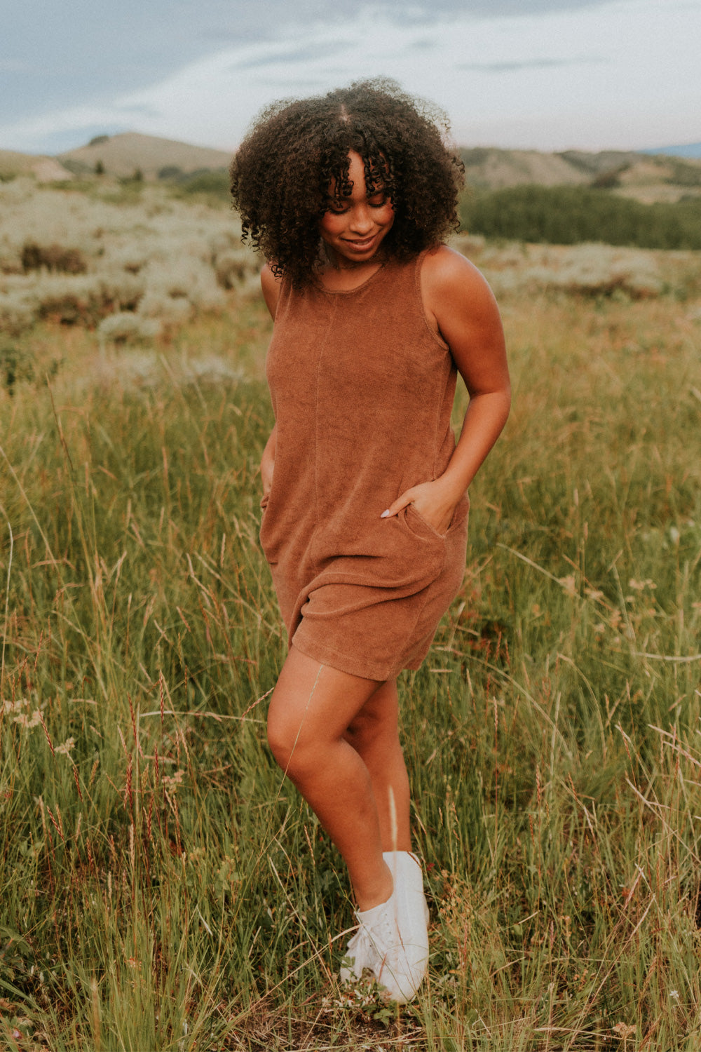 A stylish Let Go Romper made from 100% organic cotton, featuring a unique front seam and button clasp at the back, available in Brown, Olive, and Orange.