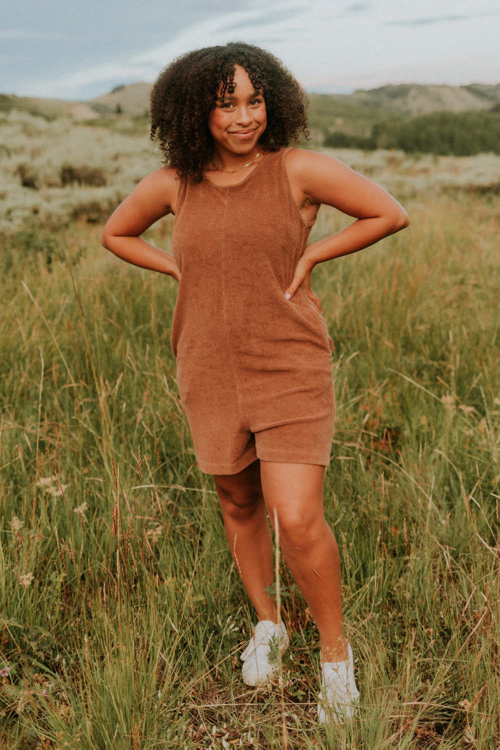 A stylish Let Go Romper made from 100% organic cotton, featuring a unique front seam and button clasp at the back, available in Brown, Olive, and Orange.