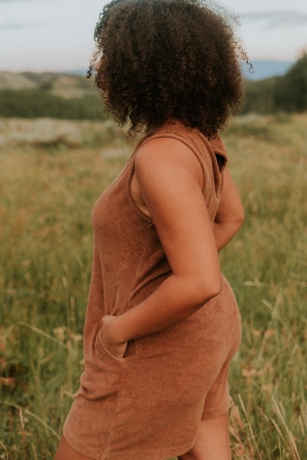 A stylish Let Go Romper made from 100% organic cotton, featuring a unique front seam and button clasp at the back, available in Brown, Olive, and Orange.