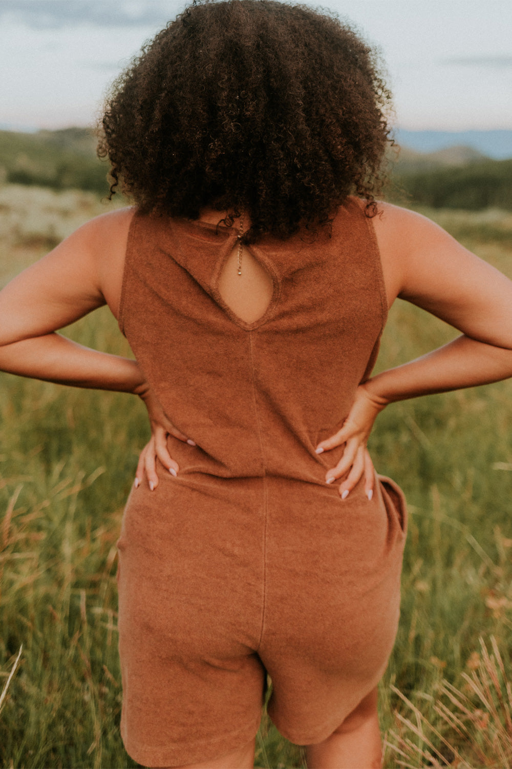 A stylish Let Go Romper made from 100% organic cotton, featuring a unique front seam and button clasp at the back, available in Brown, Olive, and Orange.