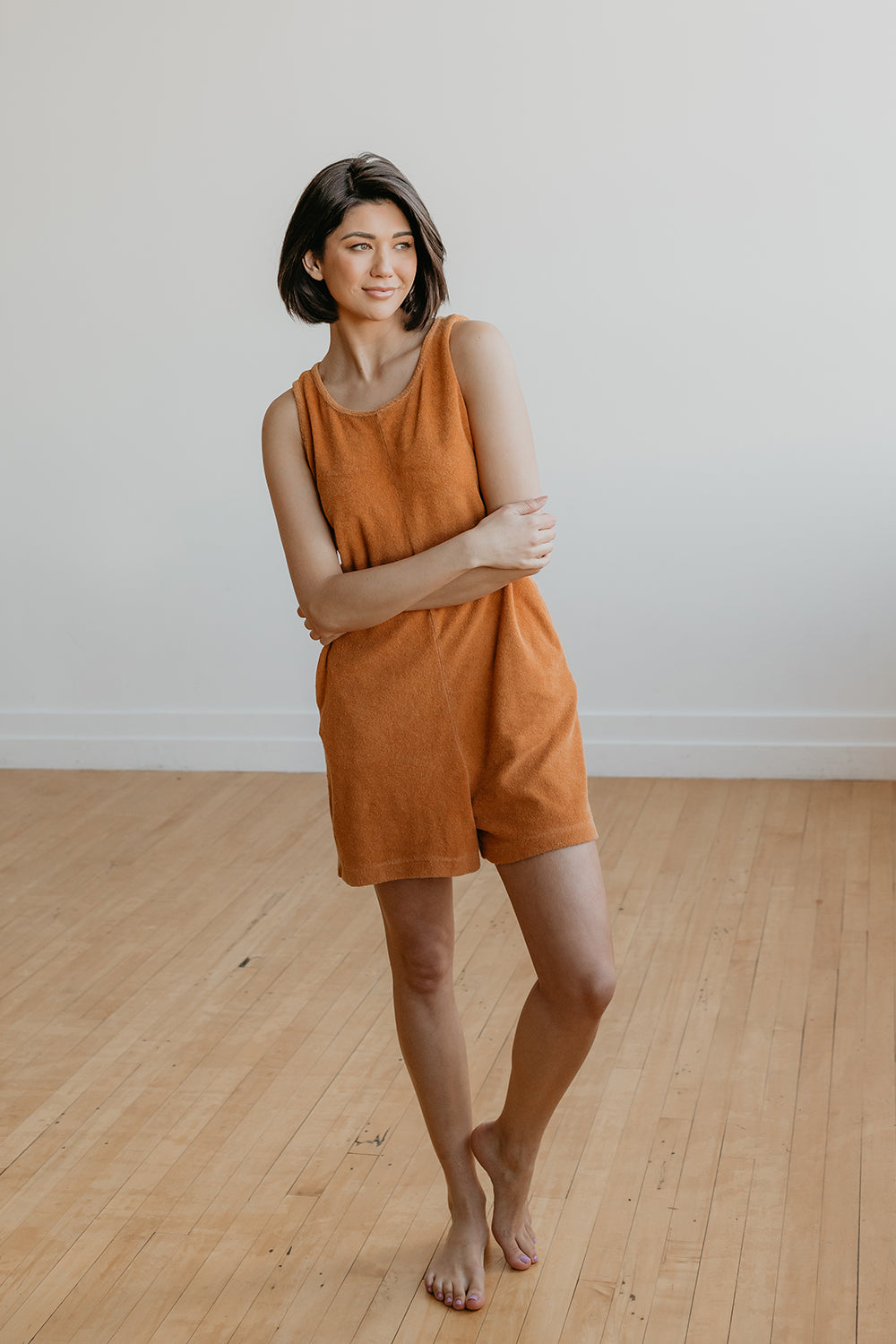 A stylish Let Go Romper made from 100% organic cotton, featuring a unique front seam and button clasp at the back, available in Brown, Olive, and Orange.