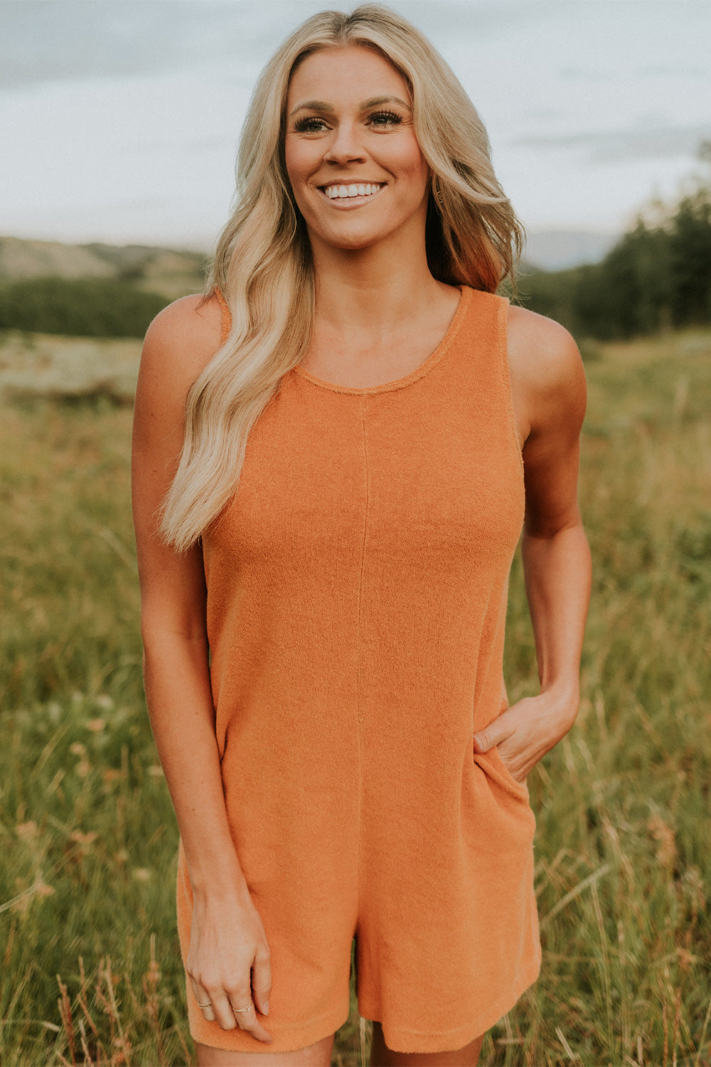 A stylish Let Go Romper made from 100% organic cotton, featuring a unique front seam and button clasp at the back, available in Brown, Olive, and Orange.