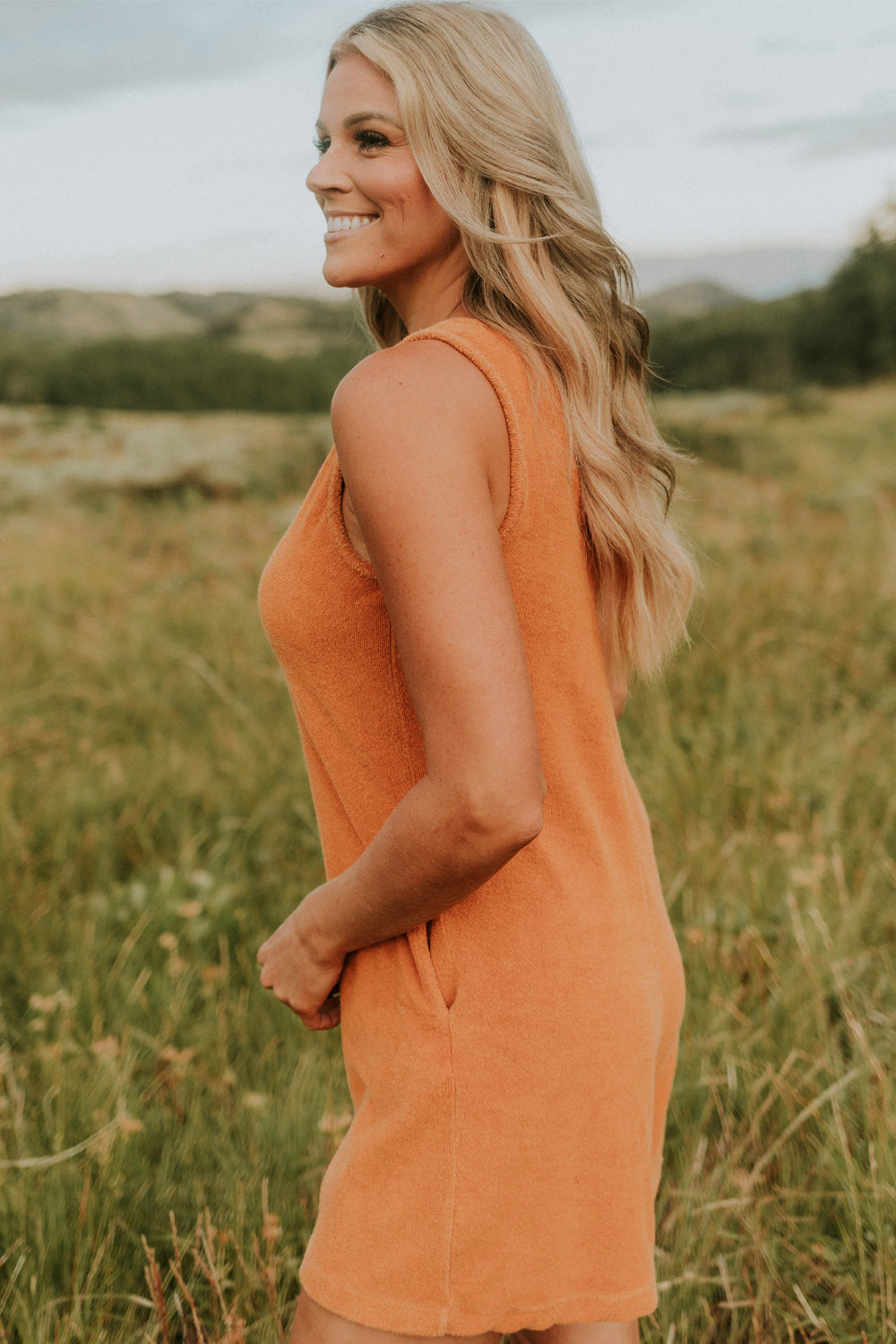 A stylish Let Go Romper made from 100% organic cotton, featuring a unique front seam and button clasp at the back, available in Brown, Olive, and Orange.