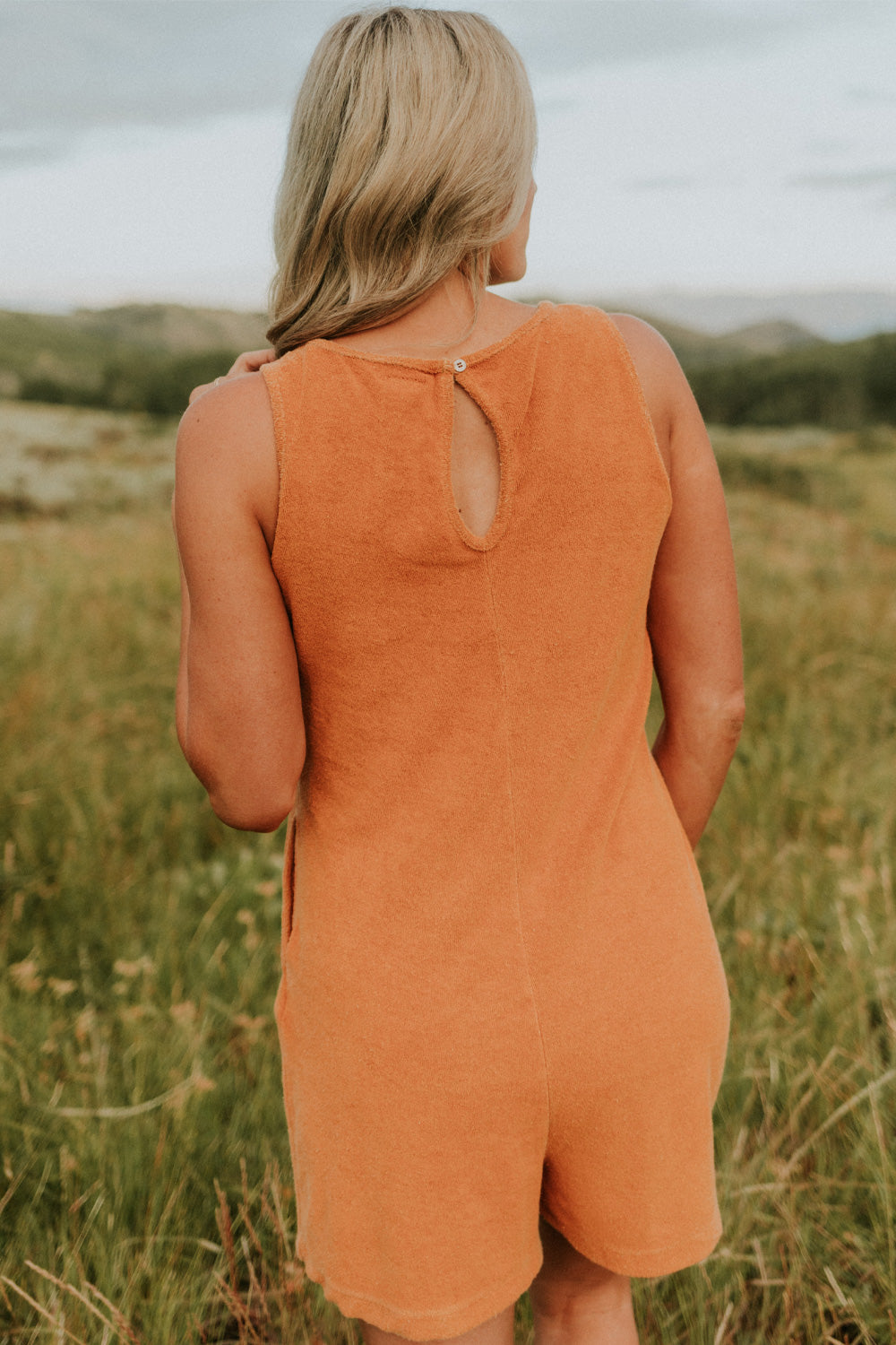 A stylish Let Go Romper made from 100% organic cotton, featuring a unique front seam and button clasp at the back, available in Brown, Olive, and Orange.