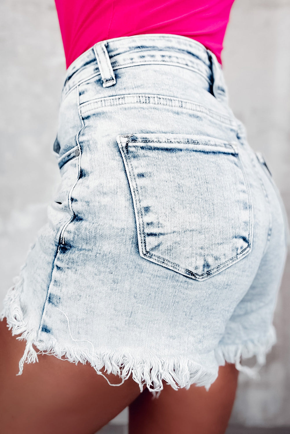 Light blue acid wash denim shorts with crossed waist and raw edge detailing, perfect for summer fashion.