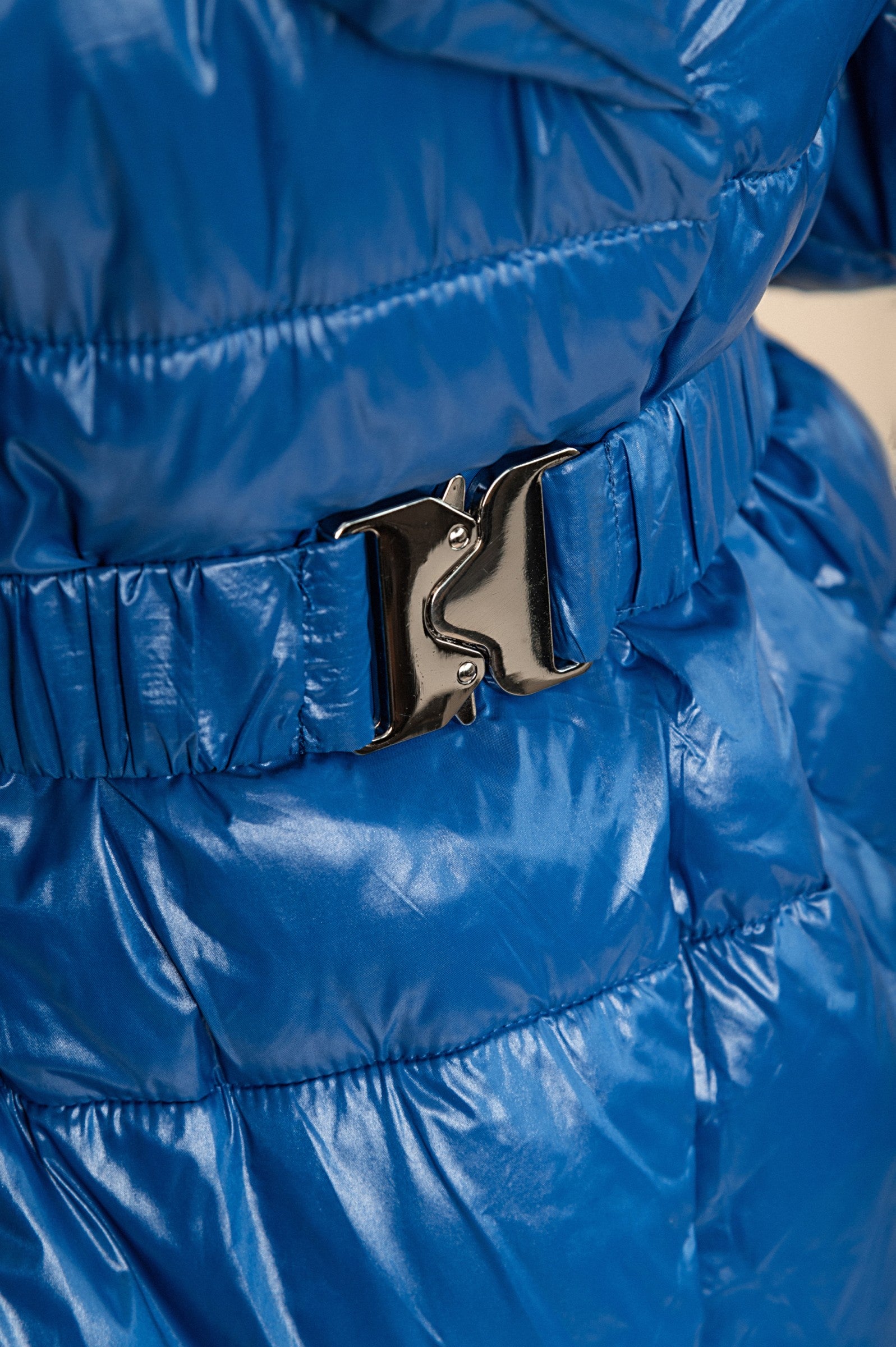 Long padded blue jacket with high collar and elastic waist, featuring a zip closure and quilted design.