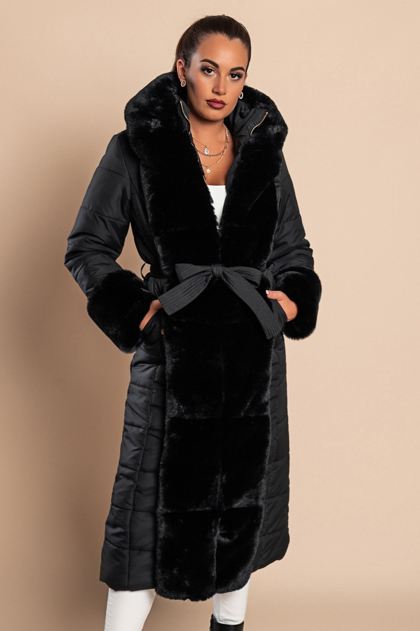 Long padded winter jacket in black with removable faux fur trim, side pockets, and metal zipper closure, designed for warmth and style.