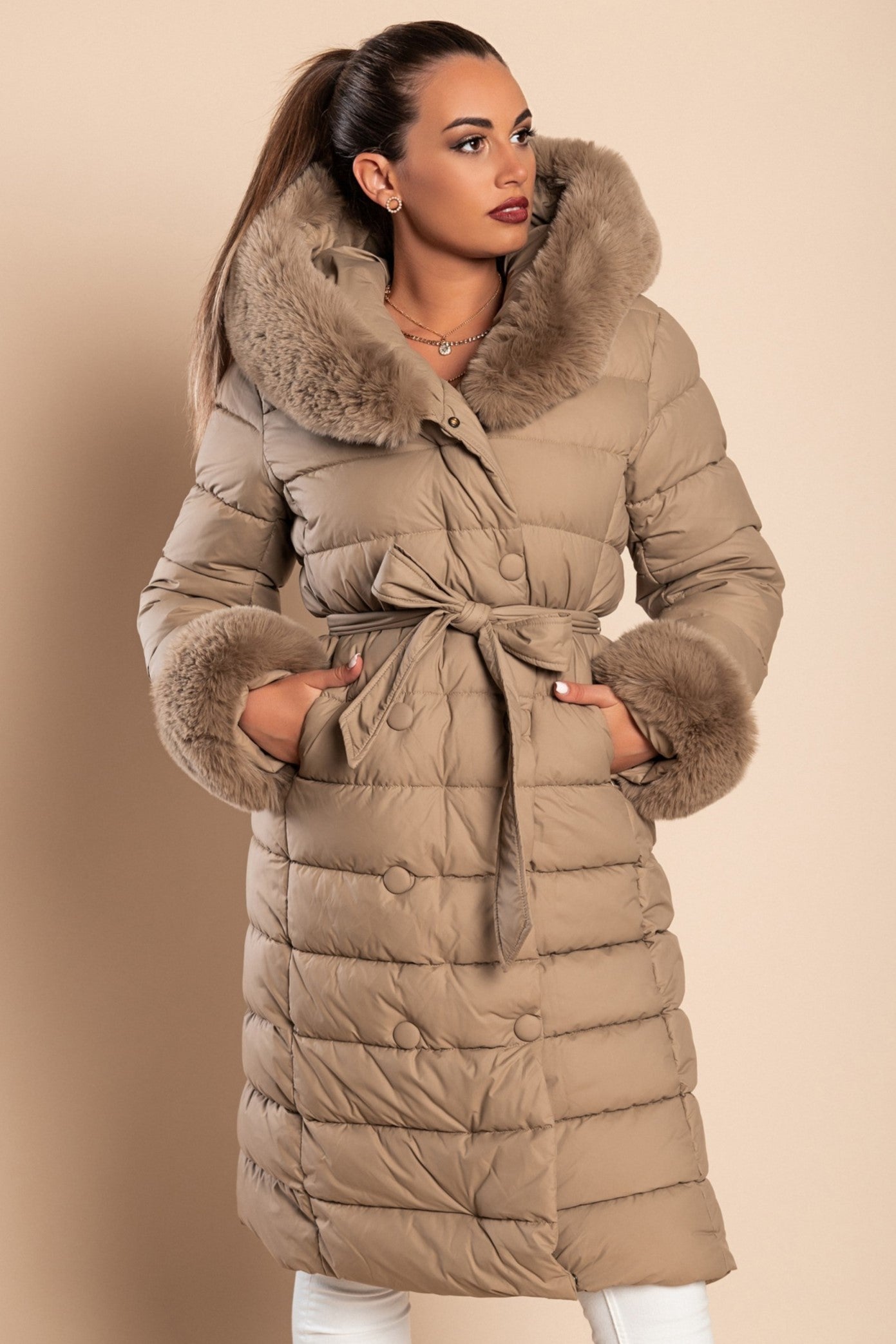 Long padded winter jacket in camel color with removable faux fur trim, side pockets, and decorative belt.