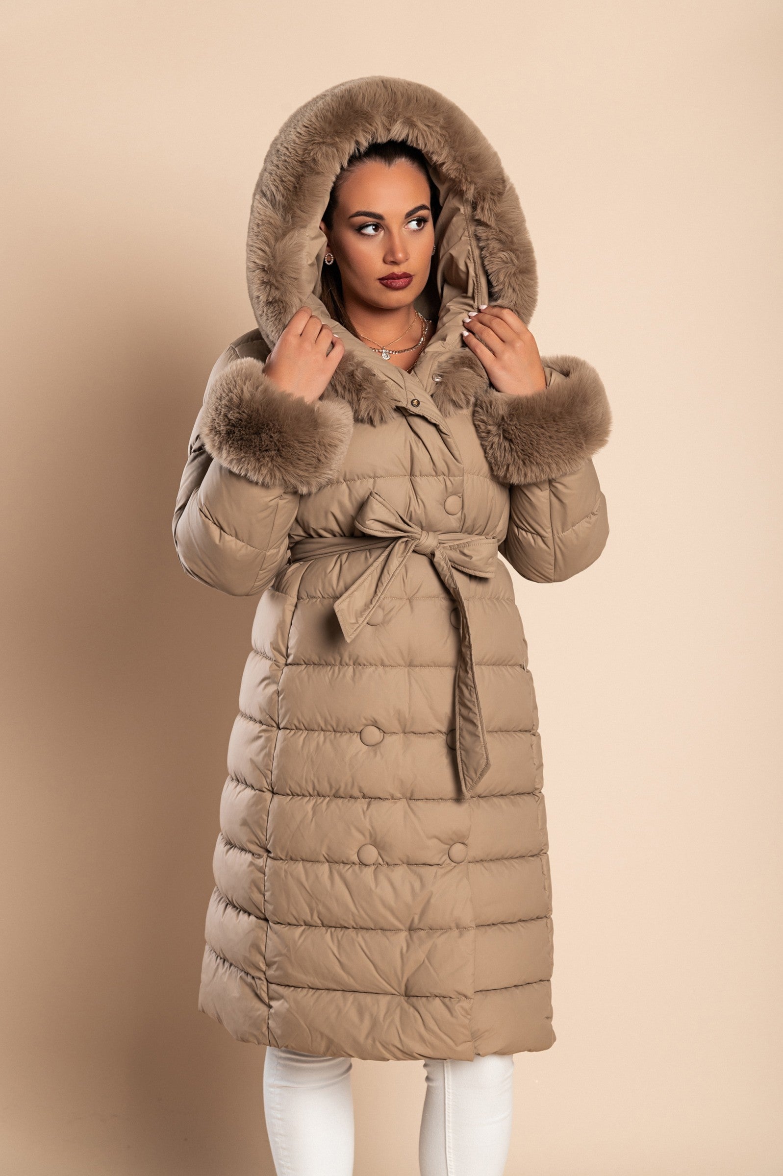 Long padded winter jacket in camel color with removable faux fur trim, side pockets, and decorative belt.