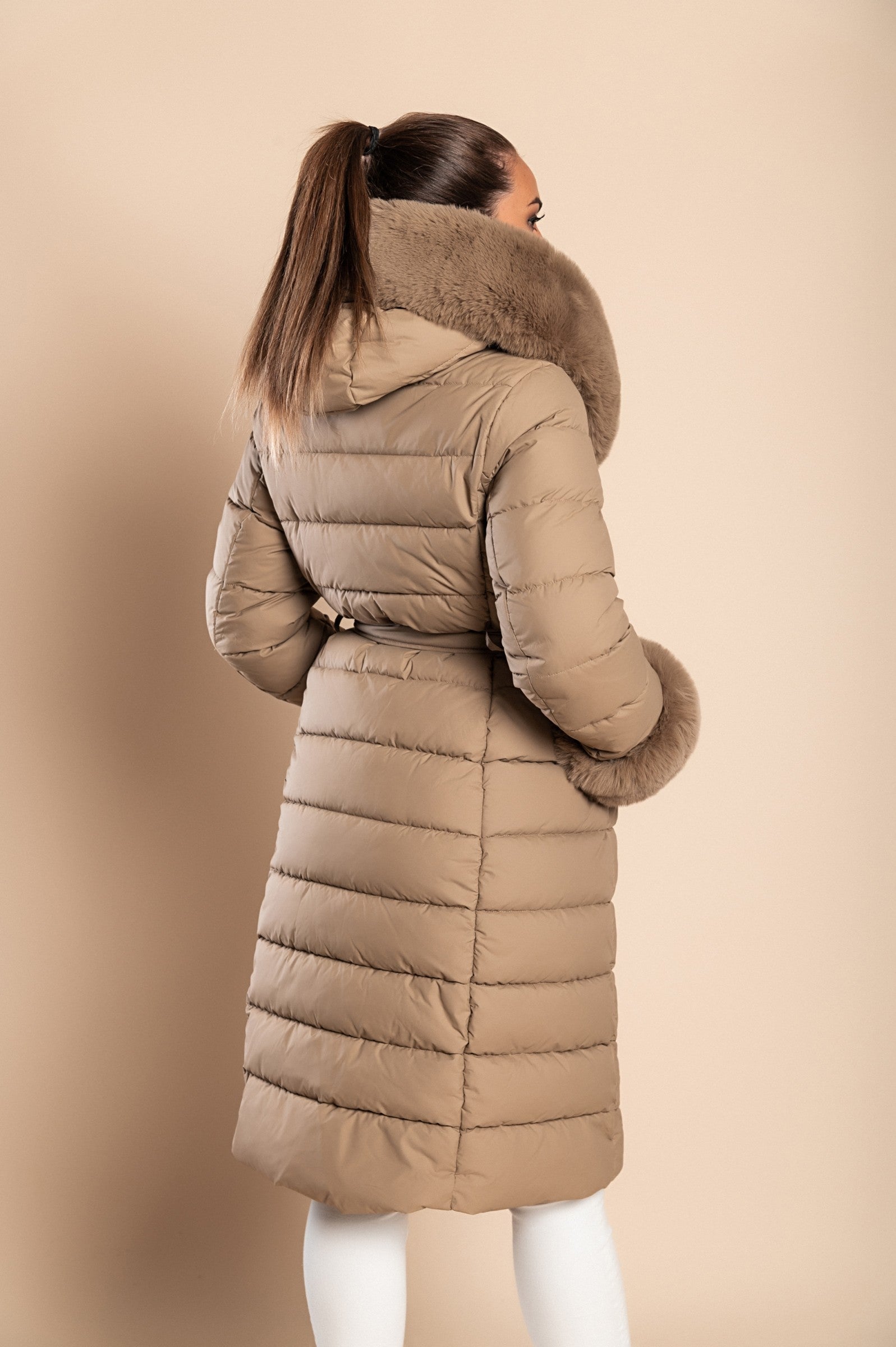 Long padded winter jacket in camel color with removable faux fur trim, side pockets, and decorative belt.