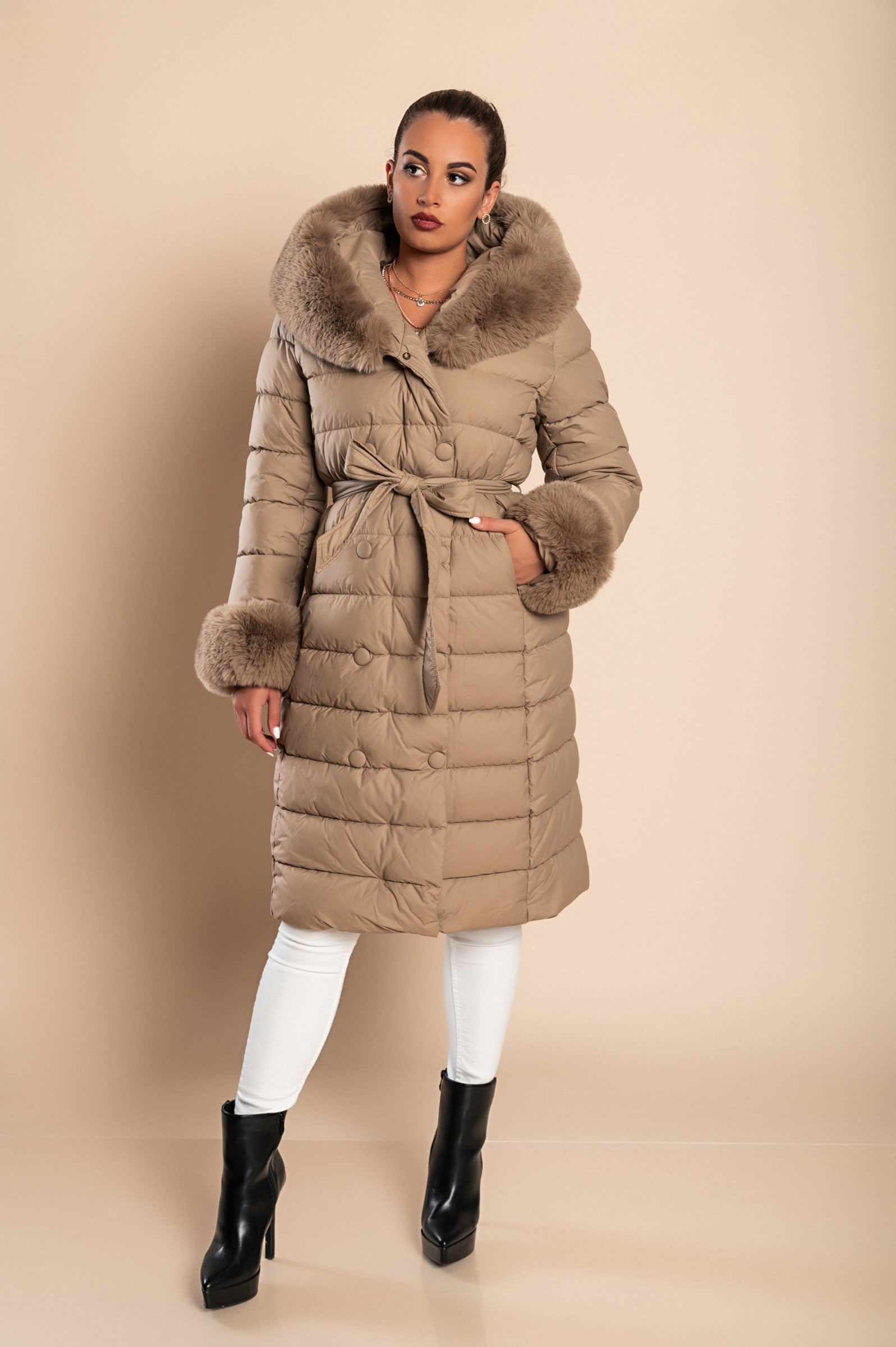 Long padded winter jacket in camel color with removable faux fur trim, side pockets, and decorative belt.