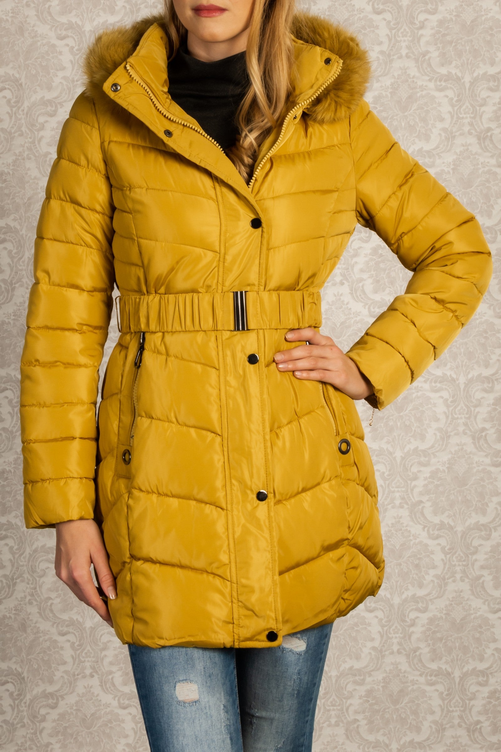 Long yellow quilted jacket with detachable faux fur hood, featuring zippered pockets and adjustable waist belt.