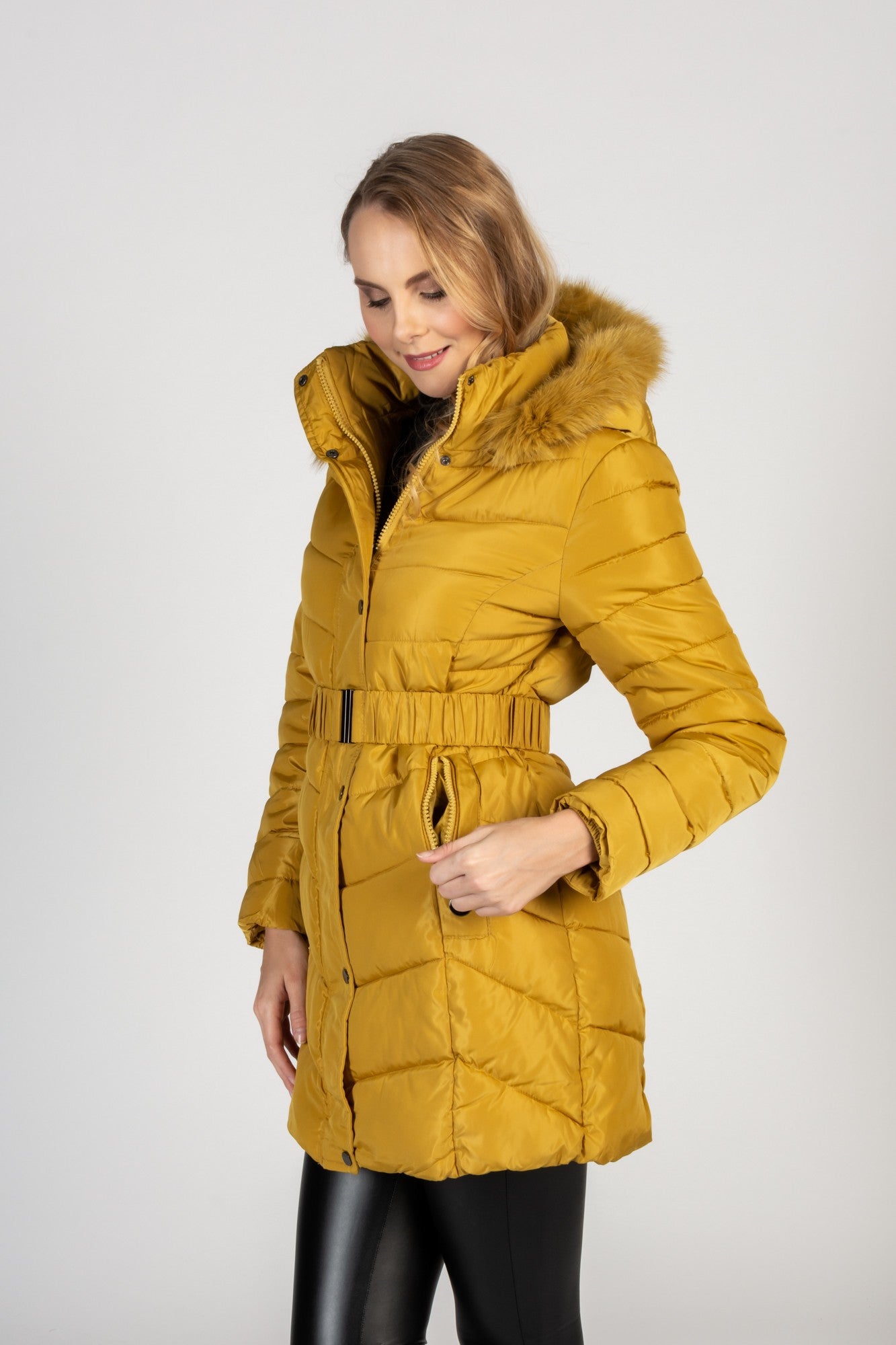 Long yellow quilted jacket with detachable faux fur hood, featuring zippered pockets and a waist belt.