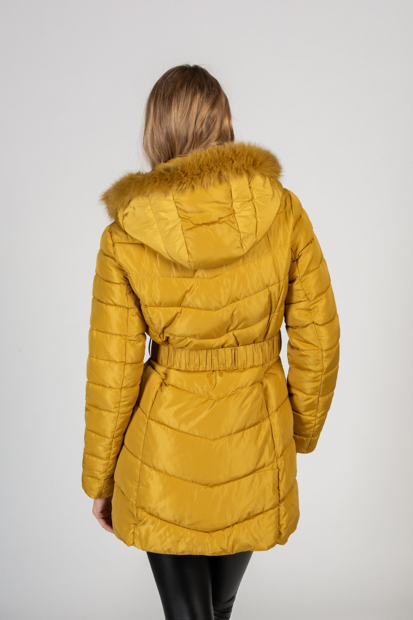 Long yellow quilted jacket with detachable faux fur hood, featuring zippered pockets and a waist belt.