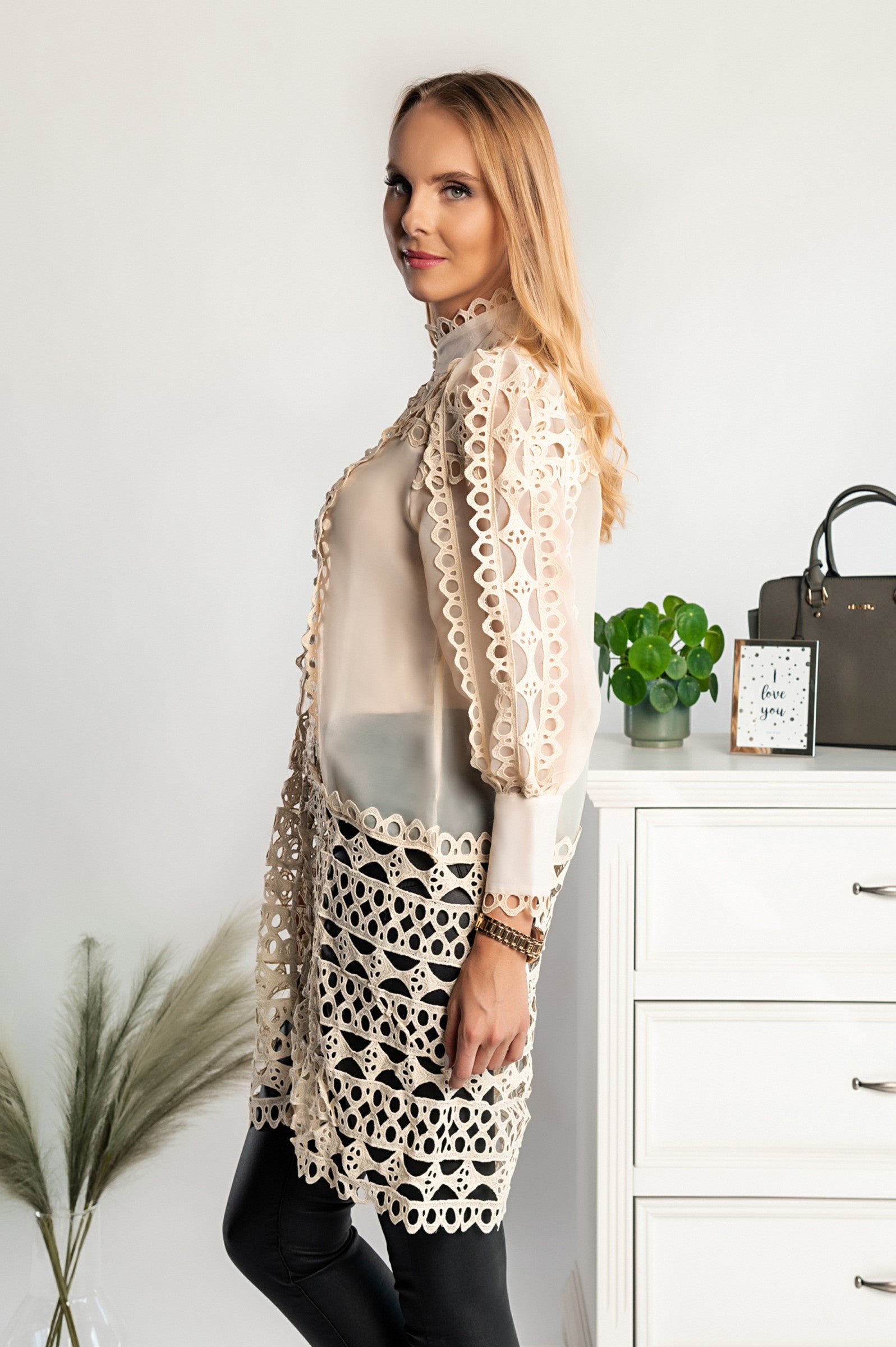 Long semi-sheer beige blouse with lace details, featuring long sleeves and a high neck, elegantly styled for a chic look.