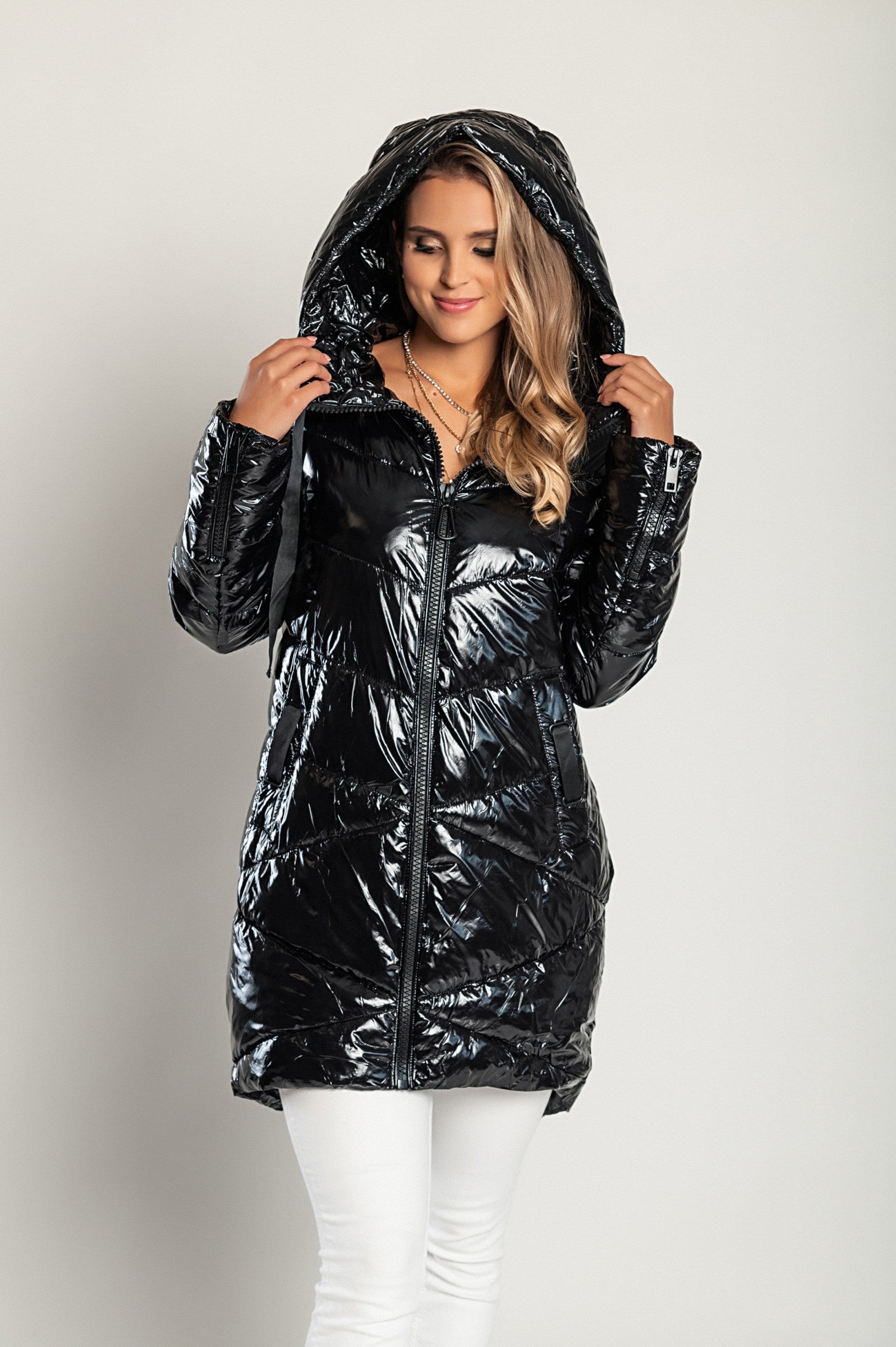 Long black winter jacket with hood, featuring a high collar and asymmetrical length, designed for warmth and style.