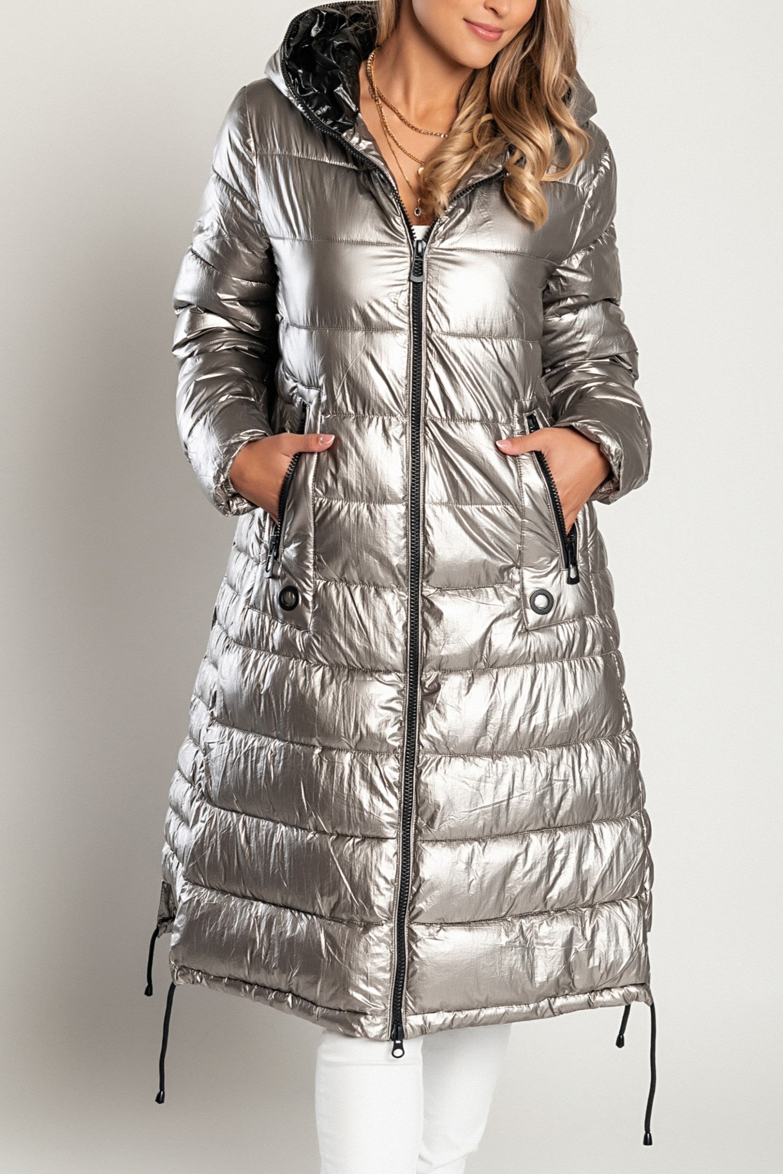 Long winter jacket with hood in silver, featuring a high collar, asymmetrical length, and side zipper pockets.