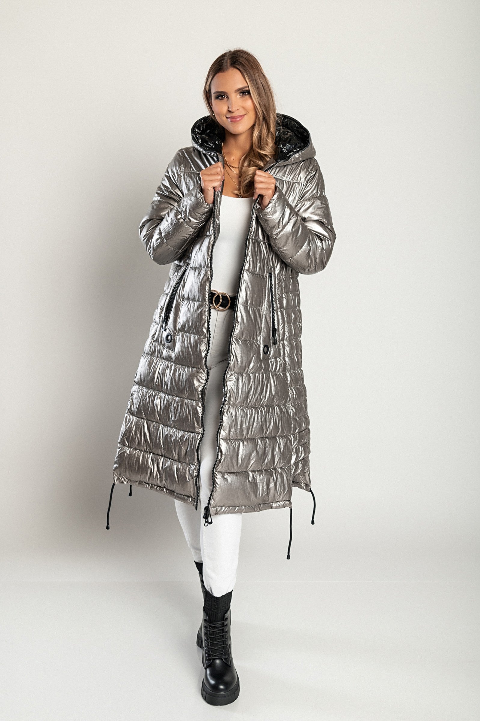 Long winter jacket with hood in silver, featuring a high collar, asymmetrical length, and side zipper pockets.