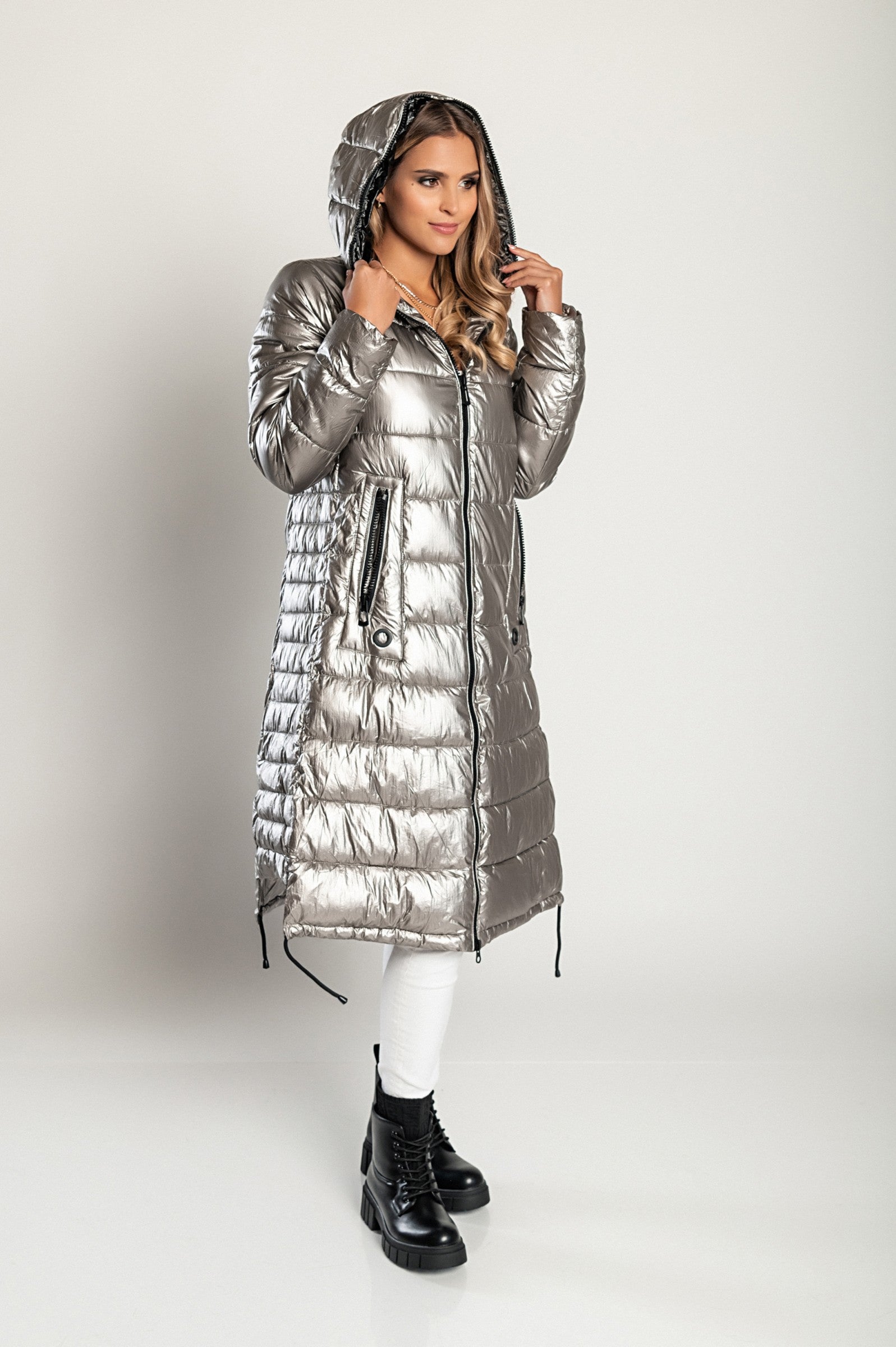 Long winter jacket with hood in silver, featuring a high collar, asymmetrical length, and side zipper pockets.