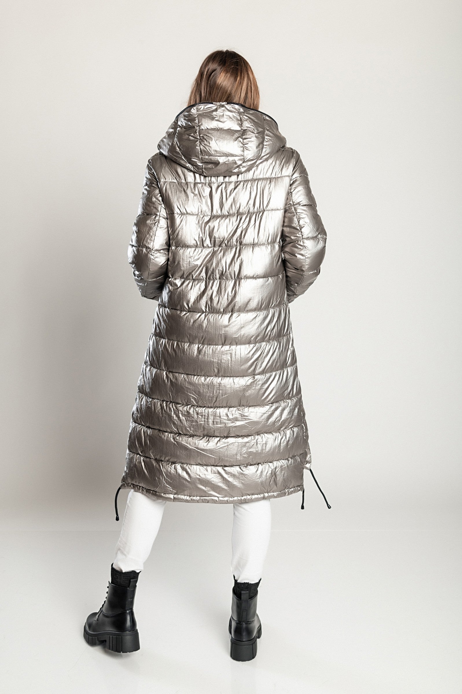 Long winter jacket with hood in silver, featuring a high collar, asymmetrical length, and side zipper pockets.