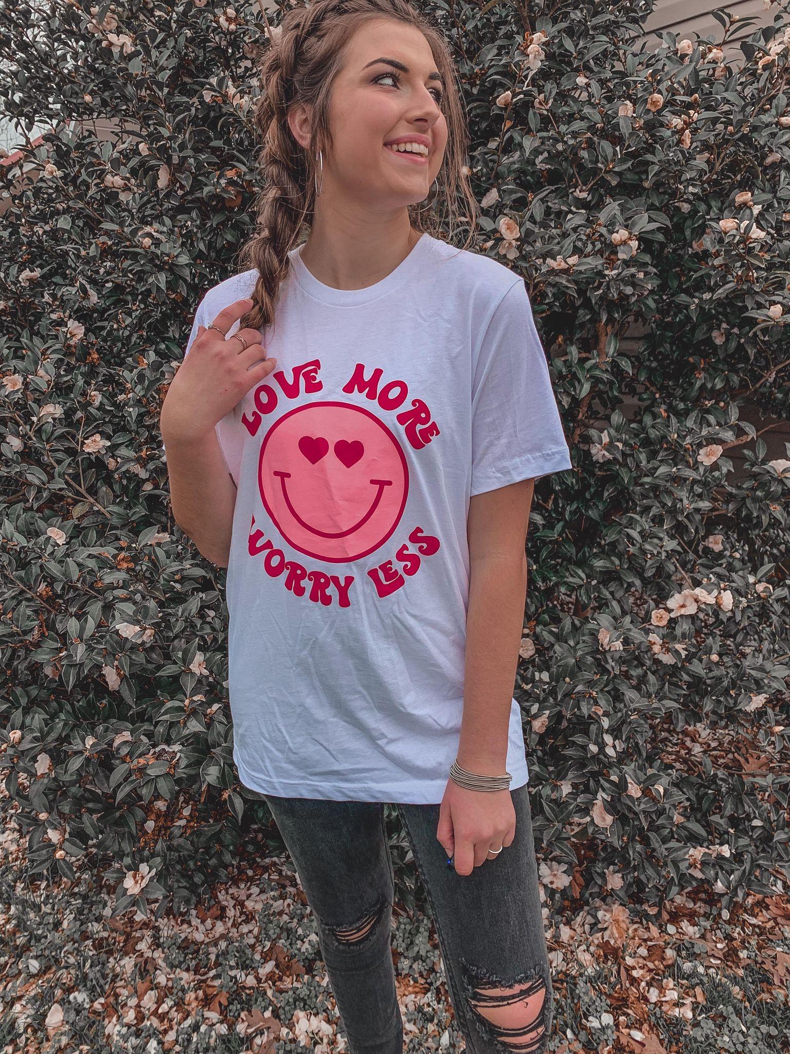 A vibrant white tee featuring the phrase 'Love More Worry Less' in colorful graphic print, showcasing a unisex design.