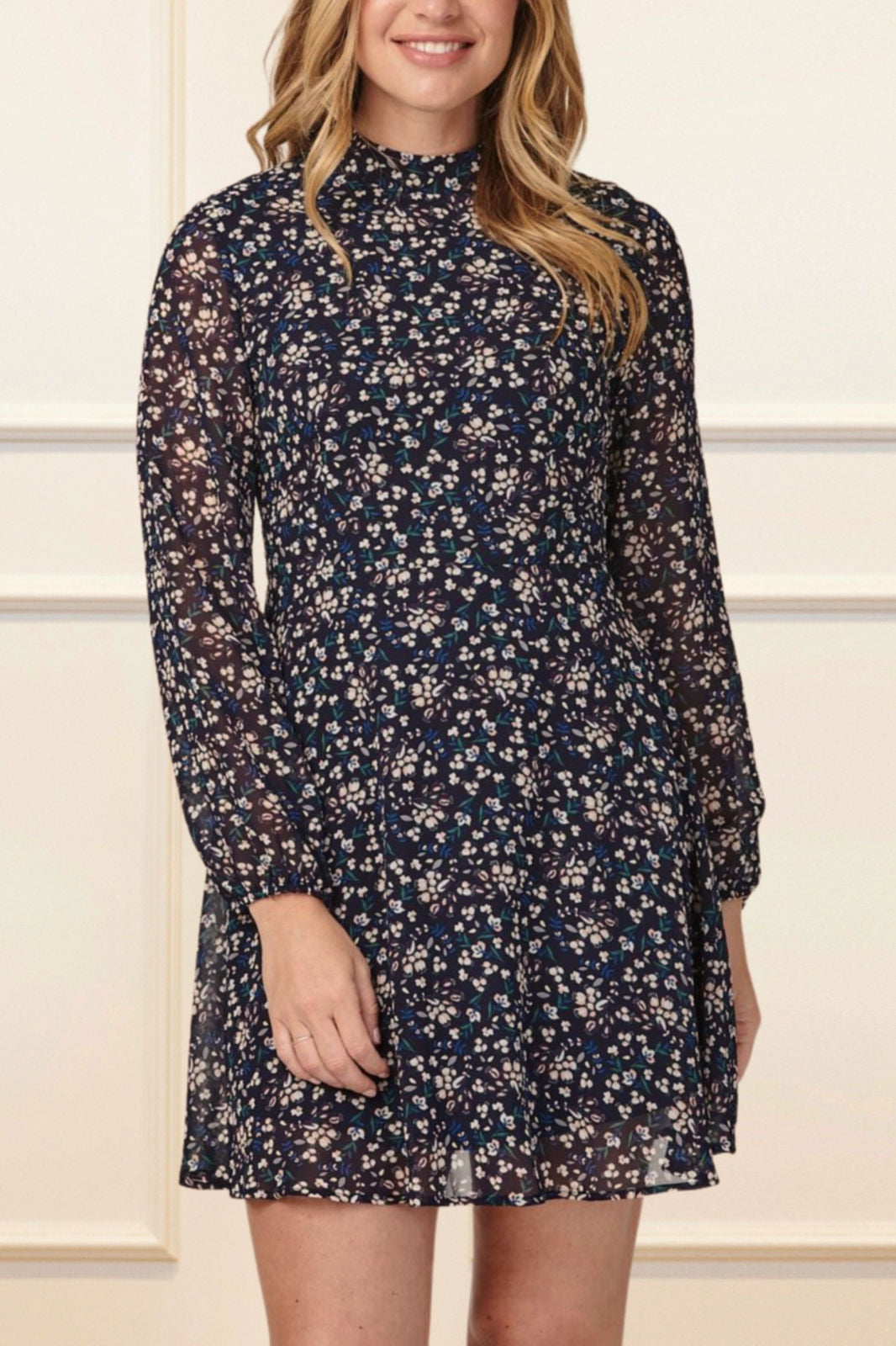 Maelys Dress featuring a short fit and flare design with a navy blue ditsy flower print, mock neck, and semi-sheer long sleeves.