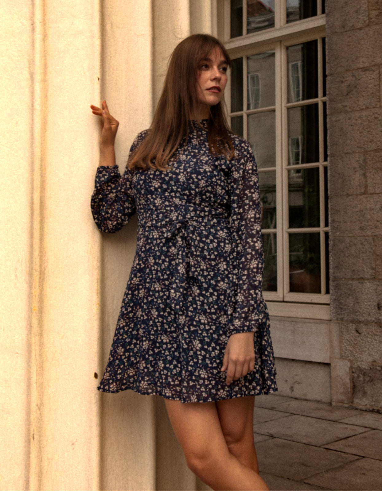 Maelys Dress featuring a short fit and flare design with a navy blue ditsy flower print, mock neck, and semi-sheer long sleeves.