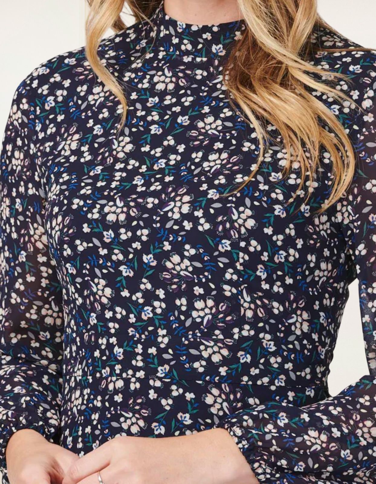 Maelys Dress featuring a short fit and flare design with a navy blue ditsy flower print, mock neck, and semi-sheer long sleeves.