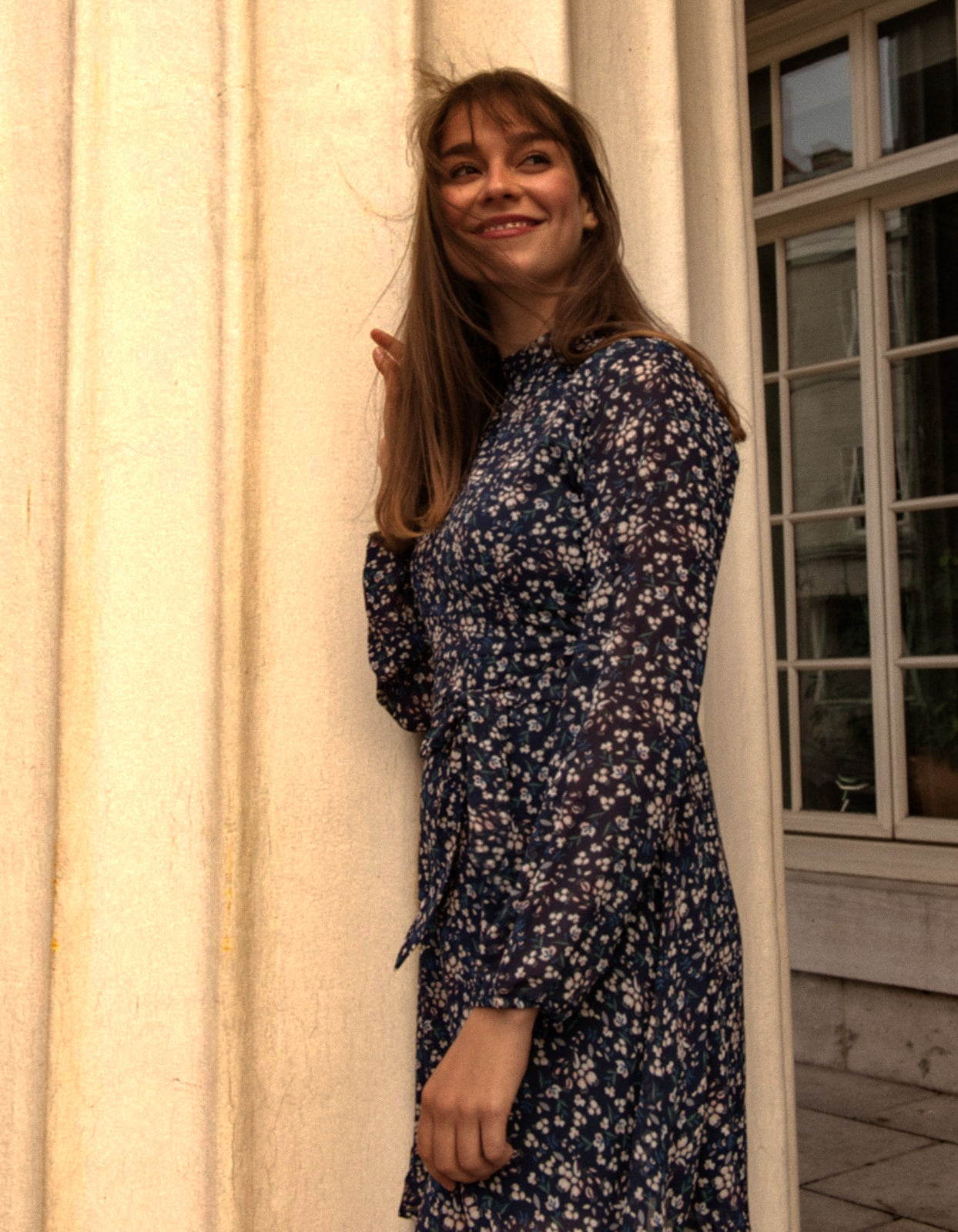 Maelys Dress featuring a short fit and flare design with a navy blue ditsy flower print, mock neck, and semi-sheer long sleeves.