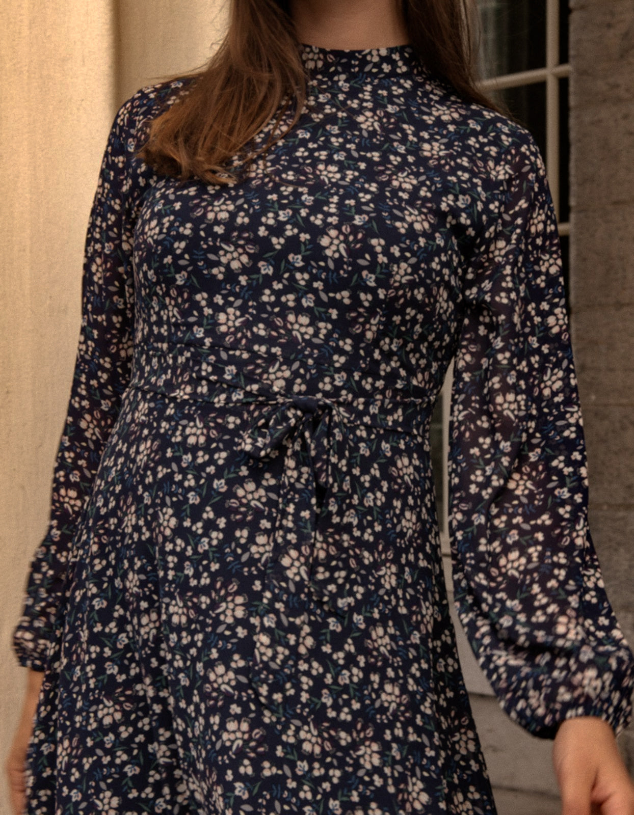 Maelys Dress featuring a short fit and flare design with a navy blue ditsy flower print, mock neck, and semi-sheer long sleeves.