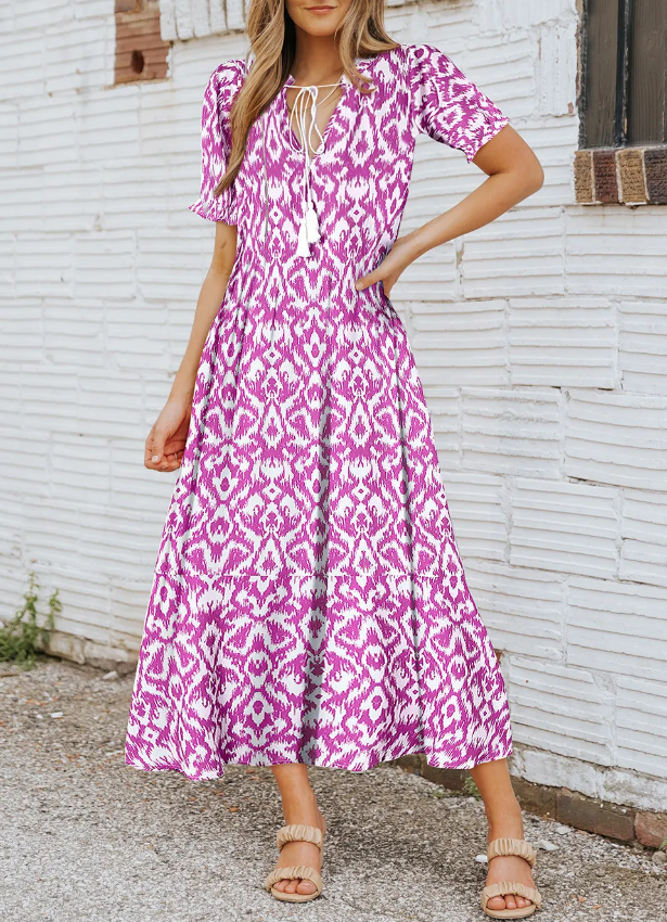 A pink maxi dress featuring a geometric print, with a V-neckline and short ruffled sleeves, flowing to ankle length.