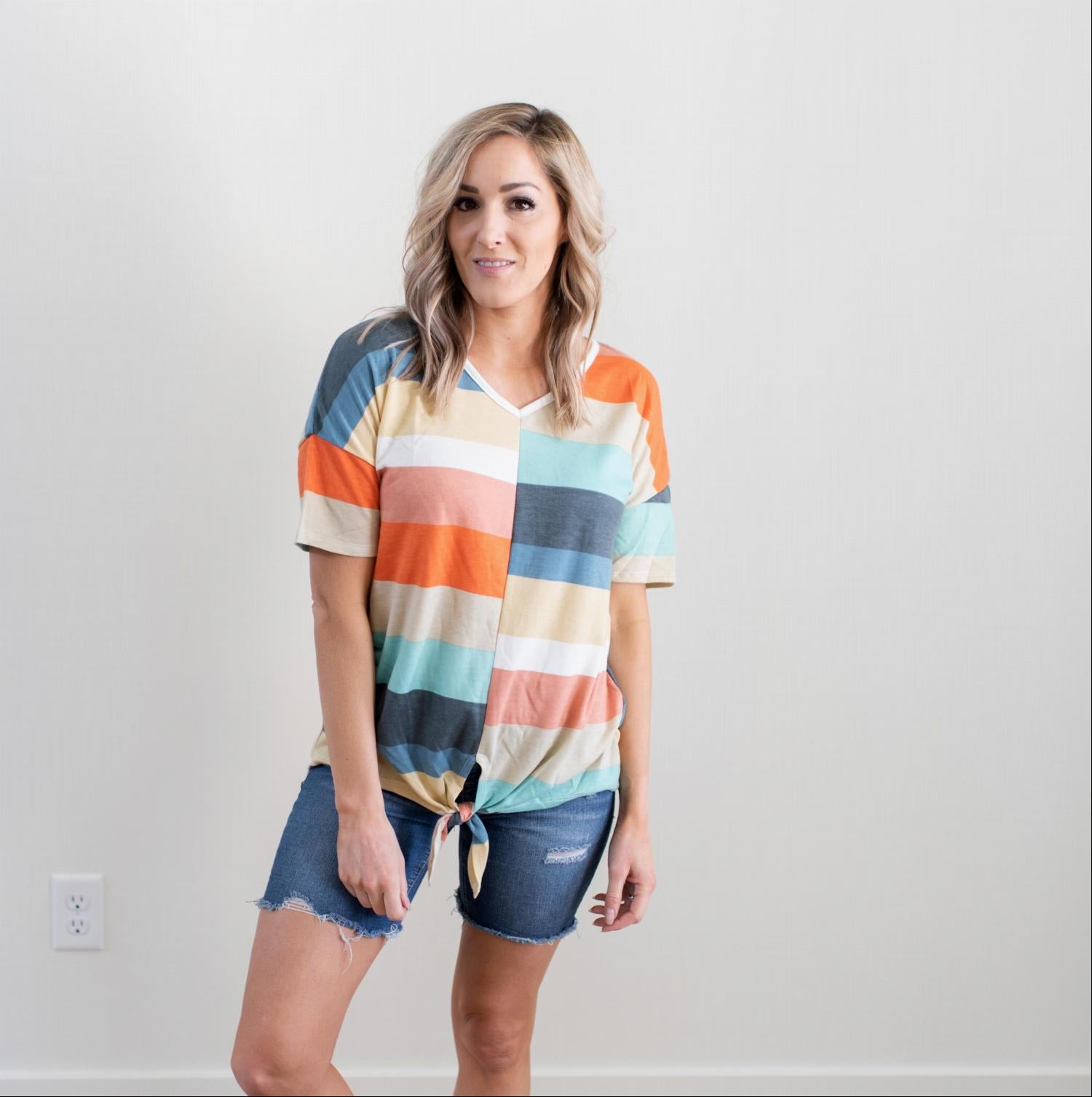 A vibrant multi-color striped short sleeve top with a trendy front tie, showcasing its stylish design and soft fabric.