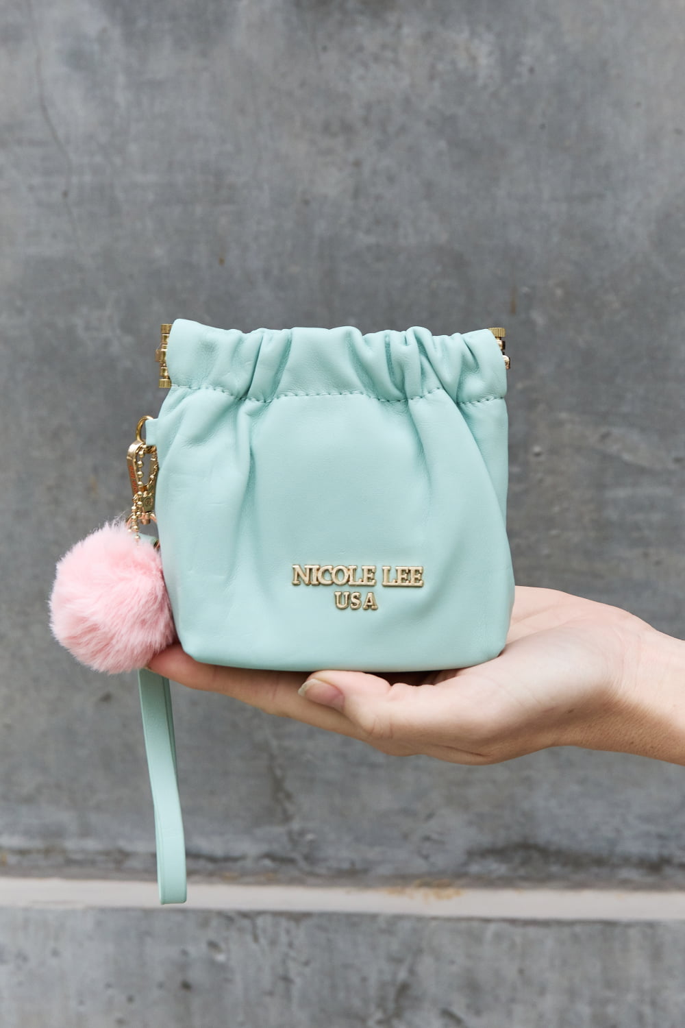 Nicole Lee USA Faux Leather Pouch in two-tone design with gold-tone hardware and detachable pompom keychain.