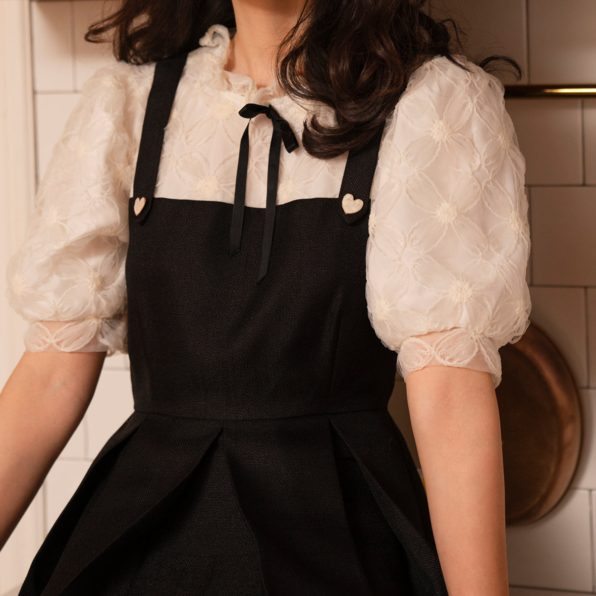 The Norah Dress featuring black tweed and floral lace, with a pleated skirt and decorative bow tie.