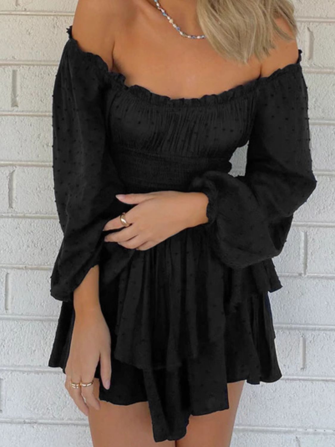 A stylish off-shoulder mini dress with a smocked waist and layered hem, featuring long sleeves and a solid pattern, perfect for casual outings.