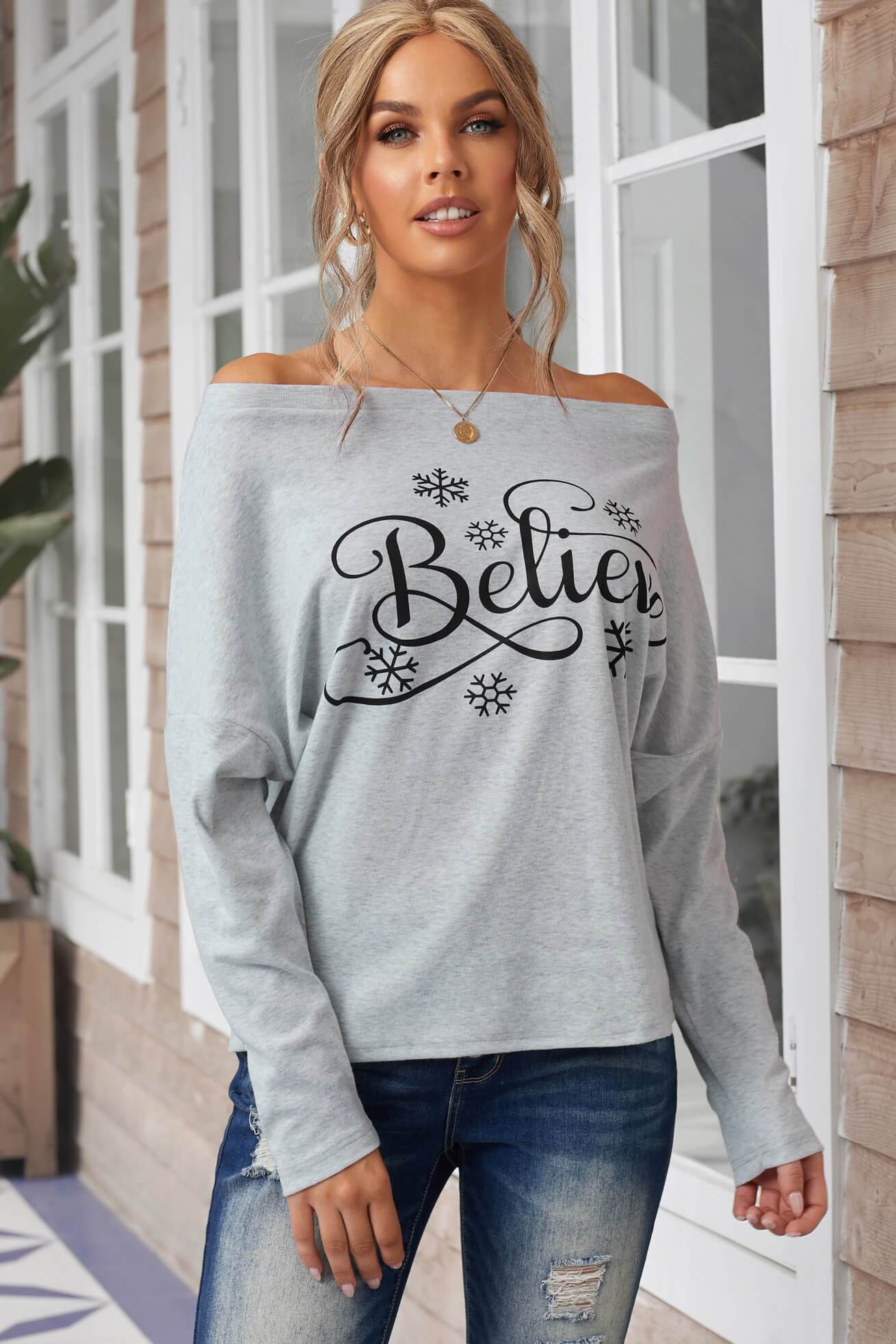 Off-the-shoulder long sleeve top featuring a snowflake pattern and 'Believe' print, perfect for holiday wear.