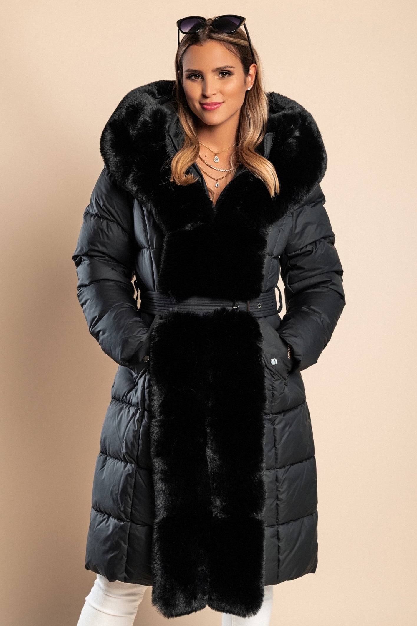 Padded black winter jacket with removable faux fur hood and decorative belt, featuring side pockets and long sleeves.