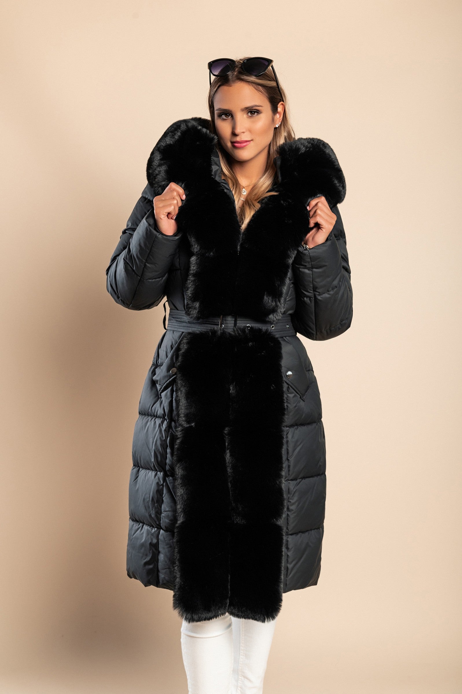 Padded black winter jacket with removable faux fur hood and decorative belt, featuring side pockets and long sleeves.