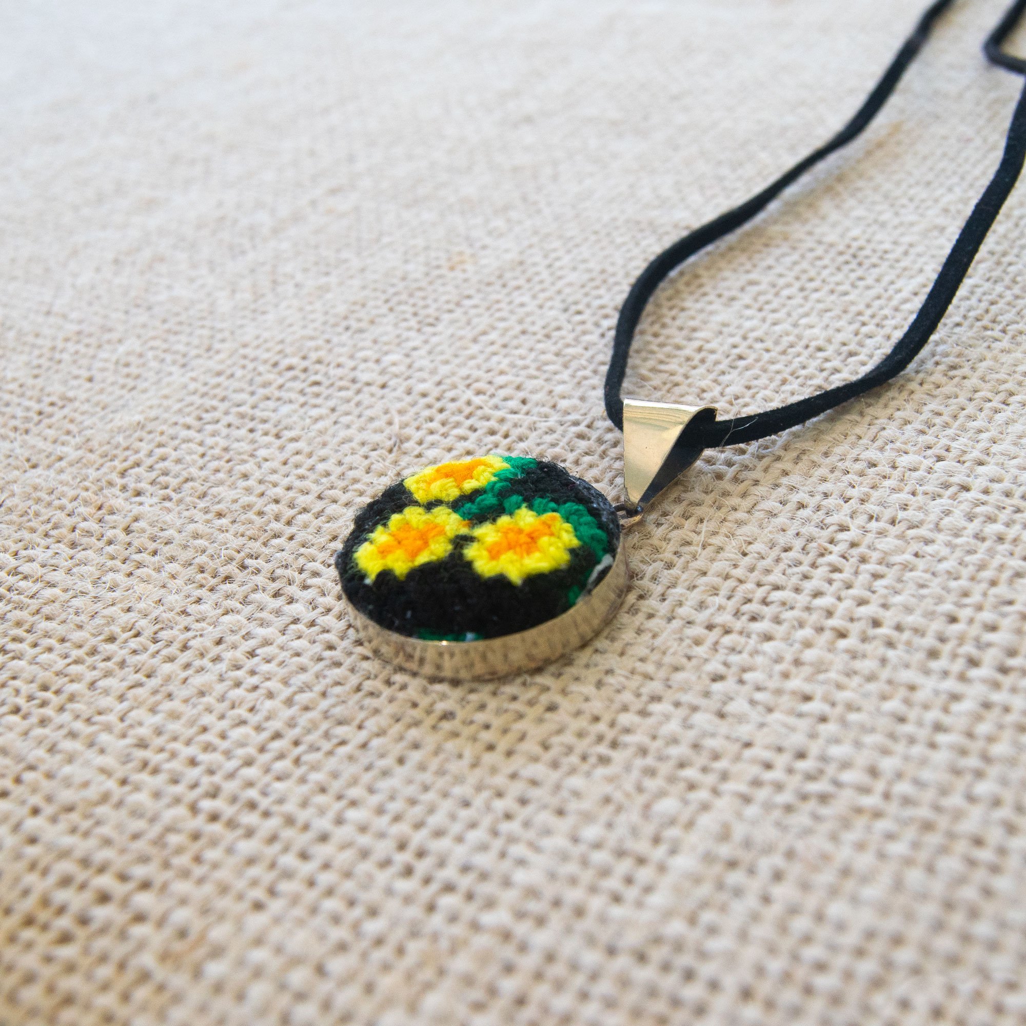 Hand embroidered circular pendant featuring vibrant yellow daisies, showcasing unique craftsmanship from Chiapas, Mexico.