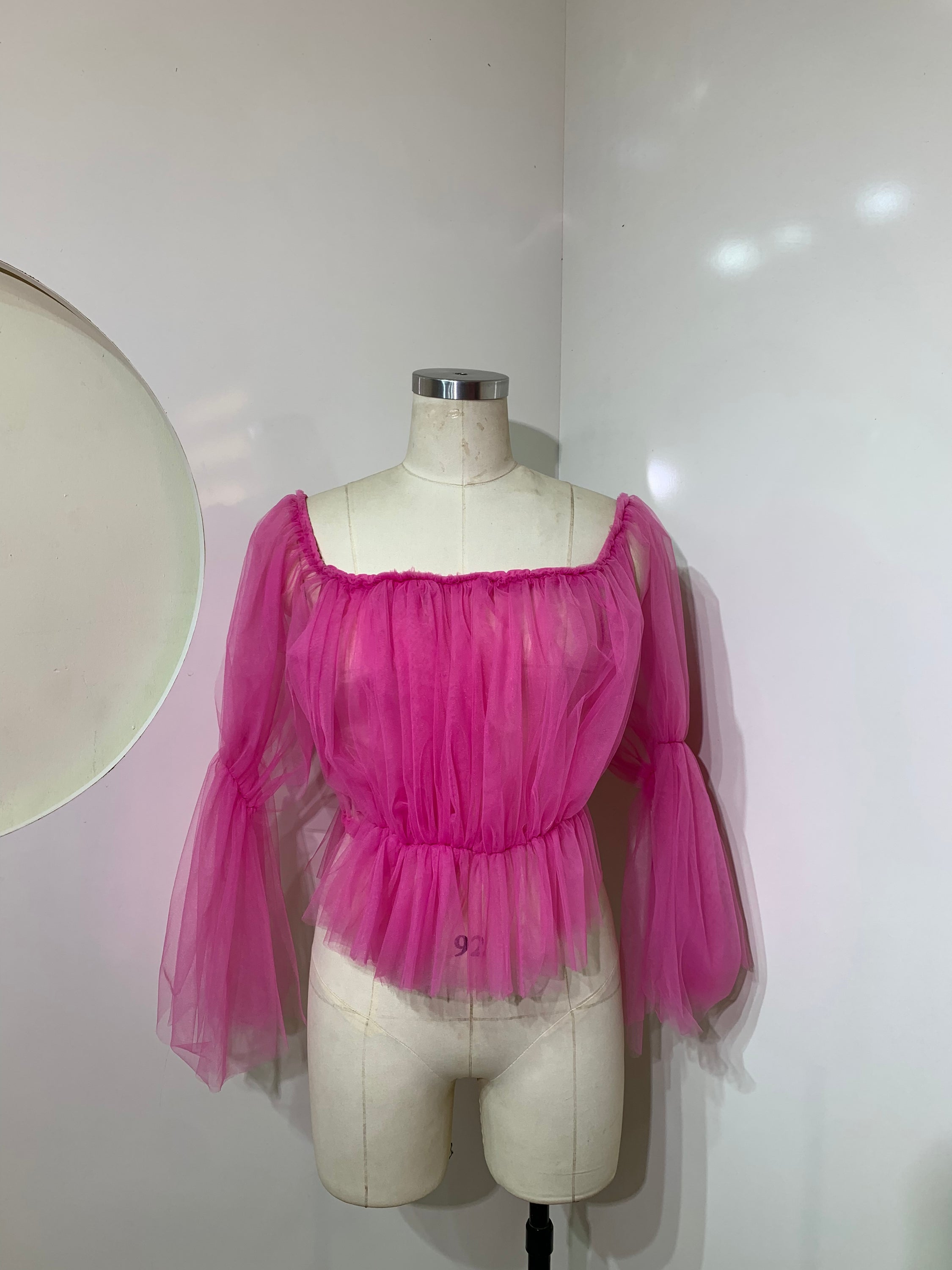 A stylish pink off-shoulder top made of delicate tulle fabric, showcasing a feminine design perfect for various occasions.