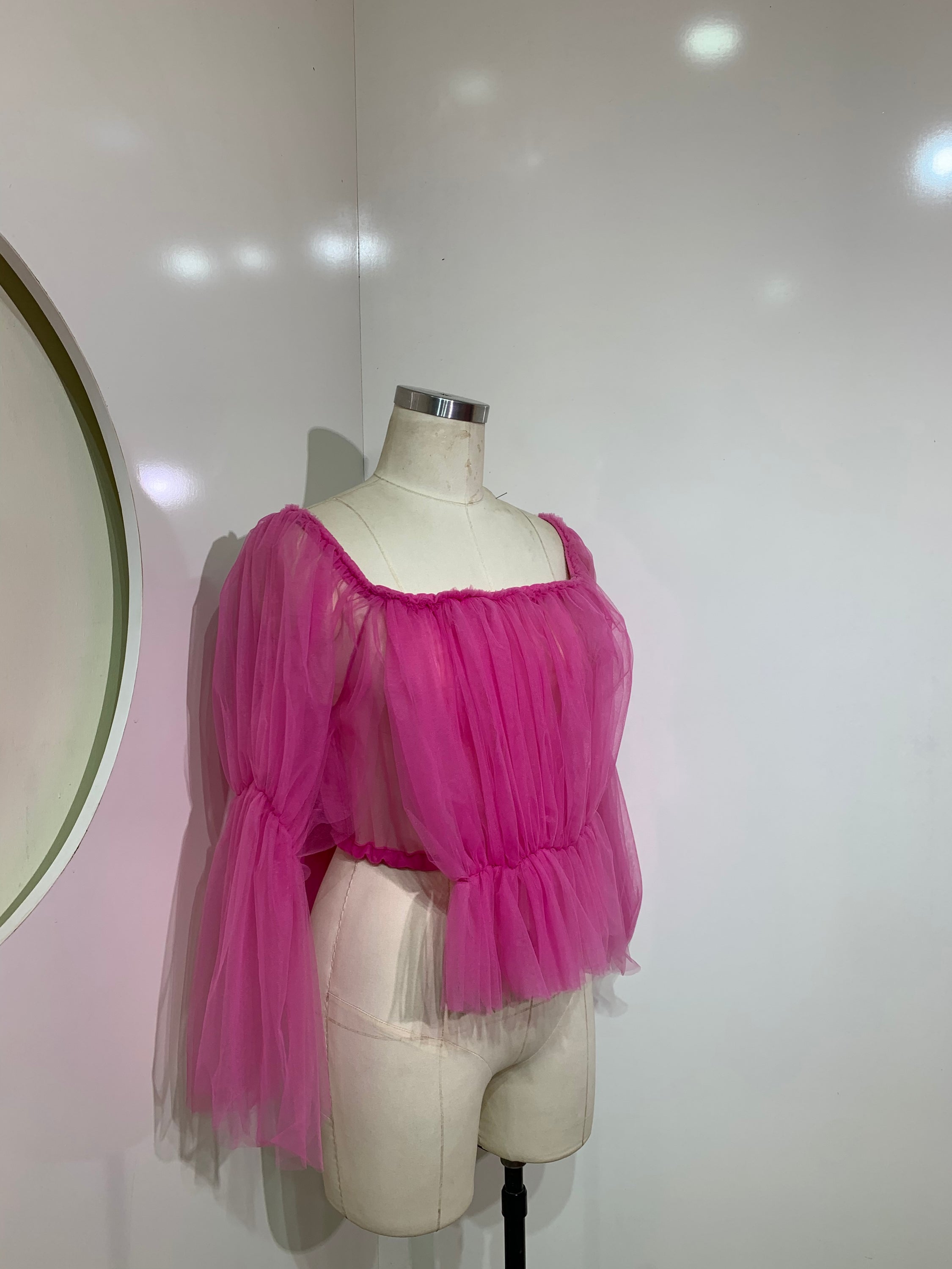 A stylish pink off-shoulder top made of delicate tulle fabric, showcasing a feminine design perfect for various occasions.