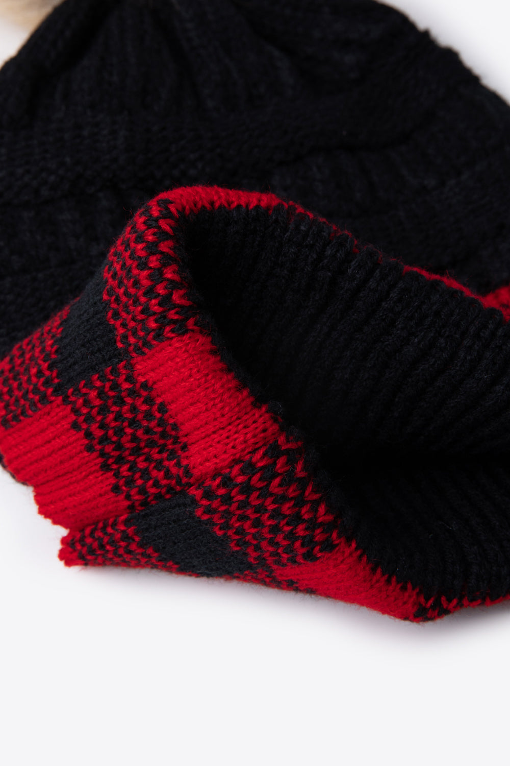 A stylish plaid pom-pom knit beanie in a flat lay style, showcasing its soft acrylic material and trendy design.