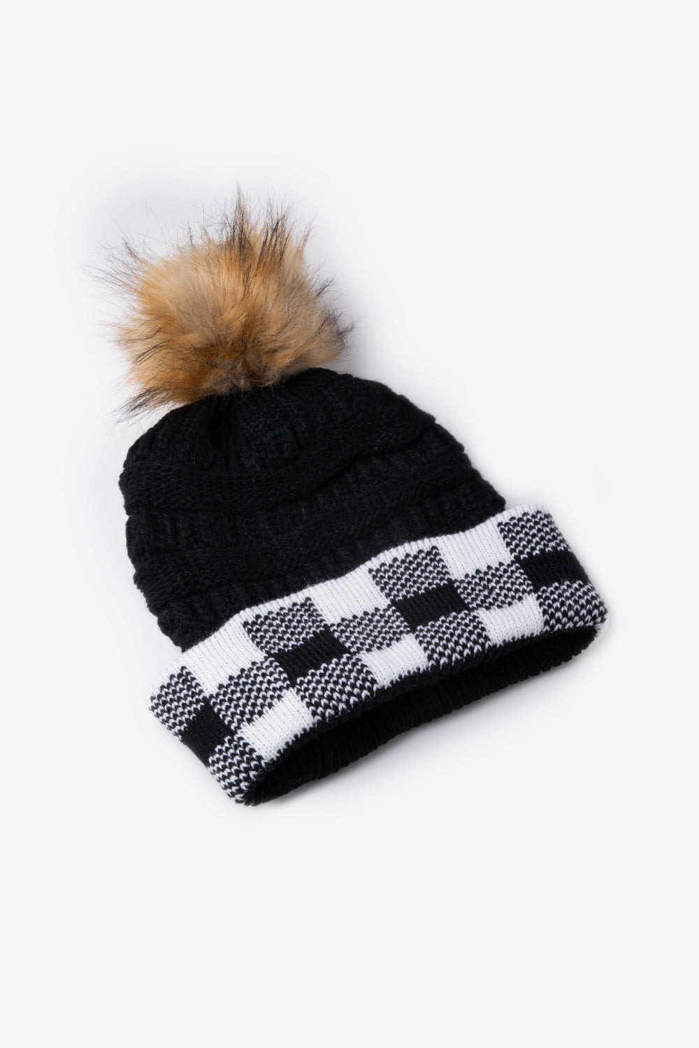 A stylish plaid pom-pom knit beanie in a flat lay style, showcasing its soft acrylic material and trendy design.